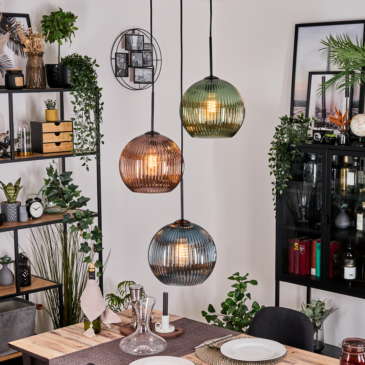 Drei Pendelleuchten mit Glaskugeln hängen über einem Holztisch. Ein Regal mit Dekoration und ein Schrank sind im Hintergrund.