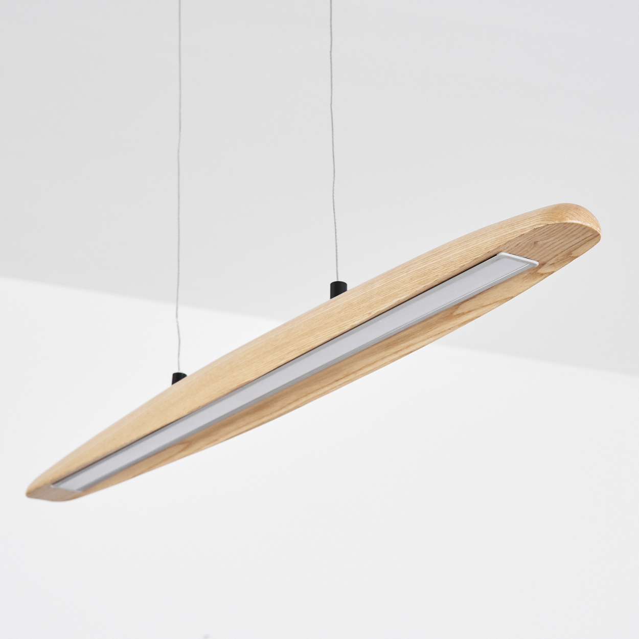 Eine moderne, längliche Holzleuchte hängt von der Decke. Sie hat einen Lichtstreifen und dunkle Haltekabel.