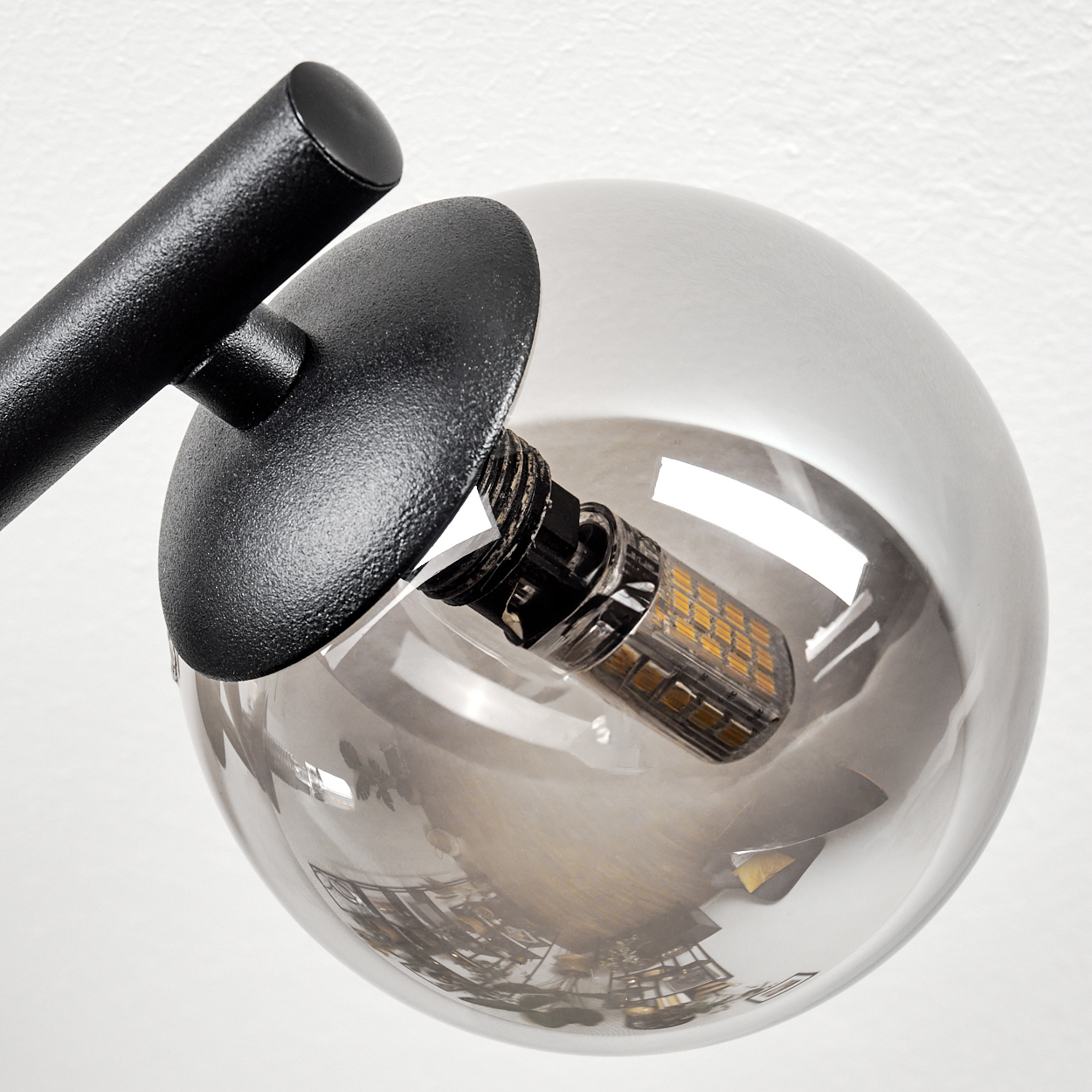 Nahaufnahme einer modernen Lampe. Sie hat einen schwarzen Metallarm und eine klare Glaskugel mit einer sichtbaren Glühbirne.