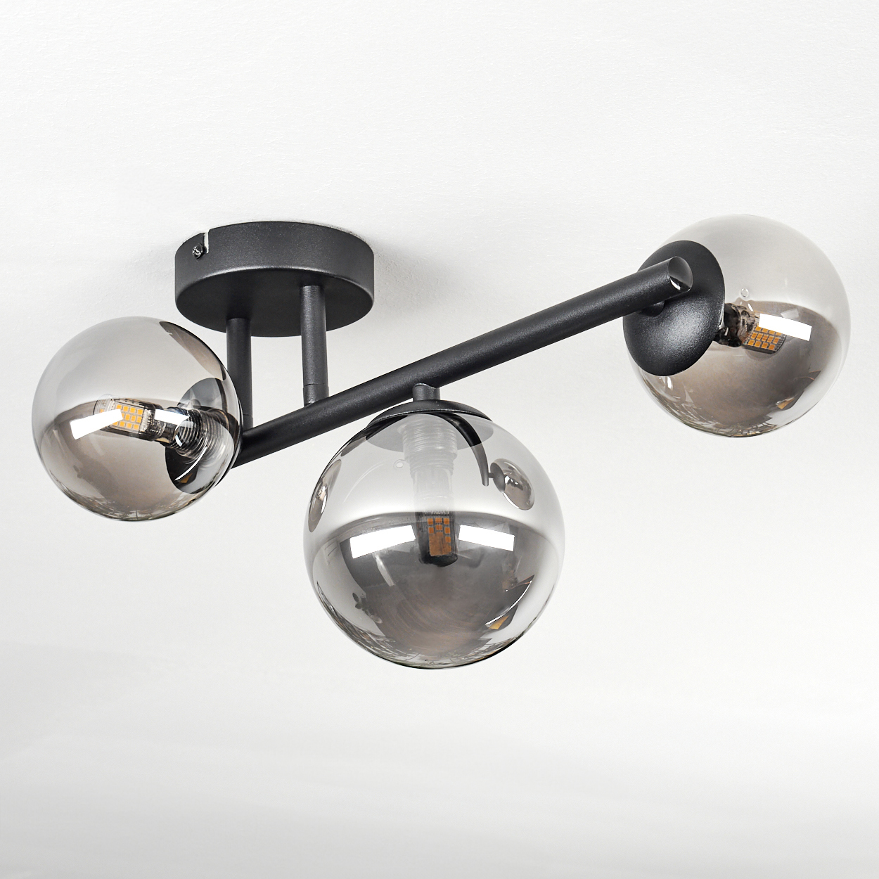 Eine moderne Deckenleuchte mit drei rauchfarbenen Glaskugeln. Schwarze Metallarme und Deckenhalterung. Der Hintergrund ist weiß.