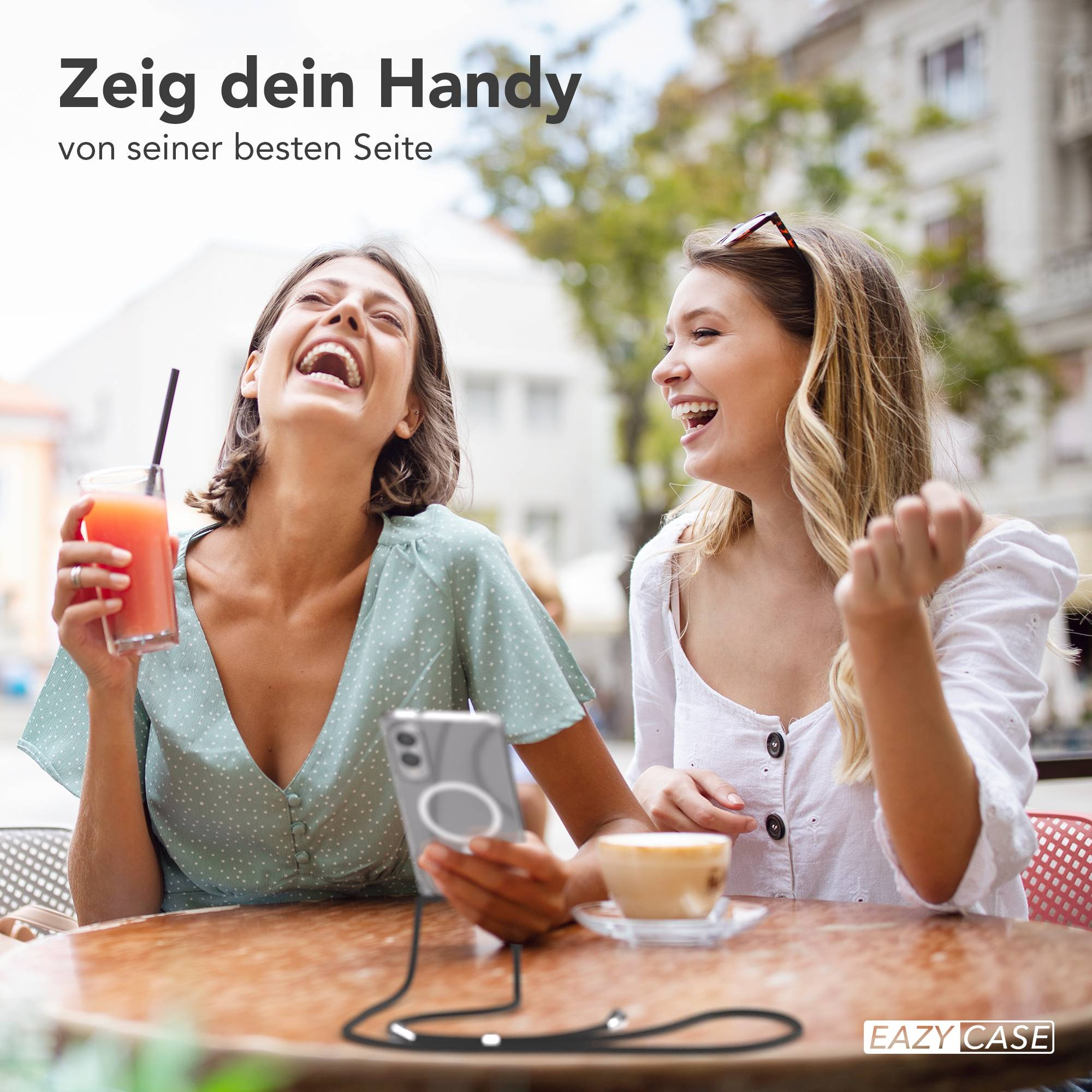 Zwei lachende Frauen, eine hält ein Getränk und ein Telefon mit Hülle. Café-Tisch-Einstellung.