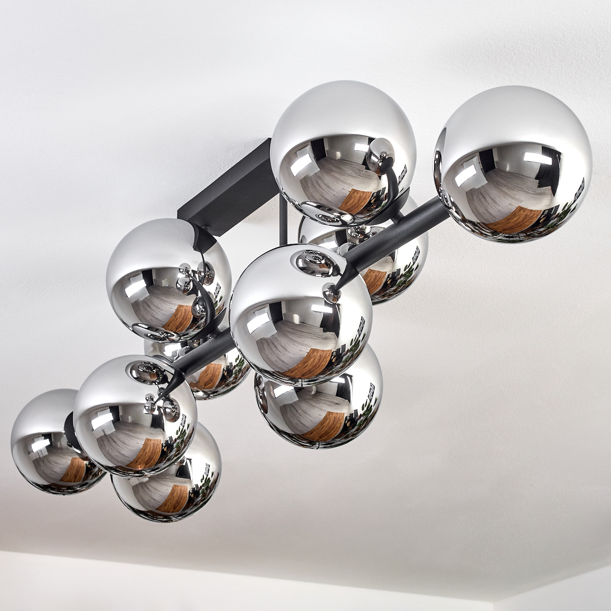 Eine moderne Deckenleuchte mit verchromten Kugeln spiegelt den Raum wider. Die Leuchte hat schwarze Arme an einer weißen Decke.