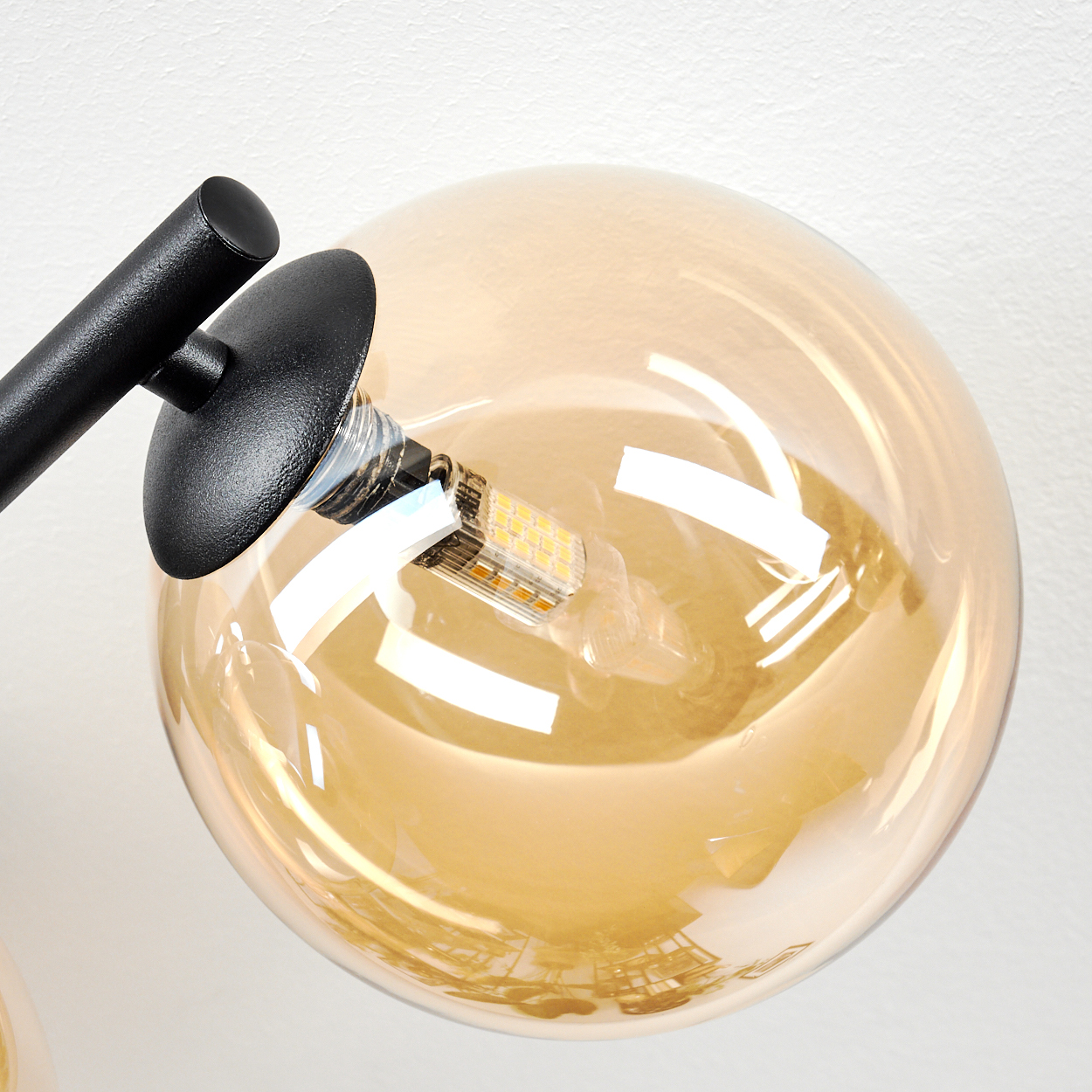 Nahaufnahme einer Leuchte. Sie hat einen schwarzen Arm und einen runden, bernsteinfarbenen Glasschirm mit einer LED-Glühbirne.