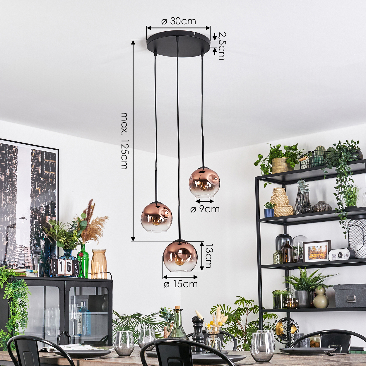 Drei kupferfarbene Pendelleuchten hängen von der Decke. Ein Esstisch mit Gläsern und ein schwarzes Metallregal mit Pflanzen sind sichtbar.