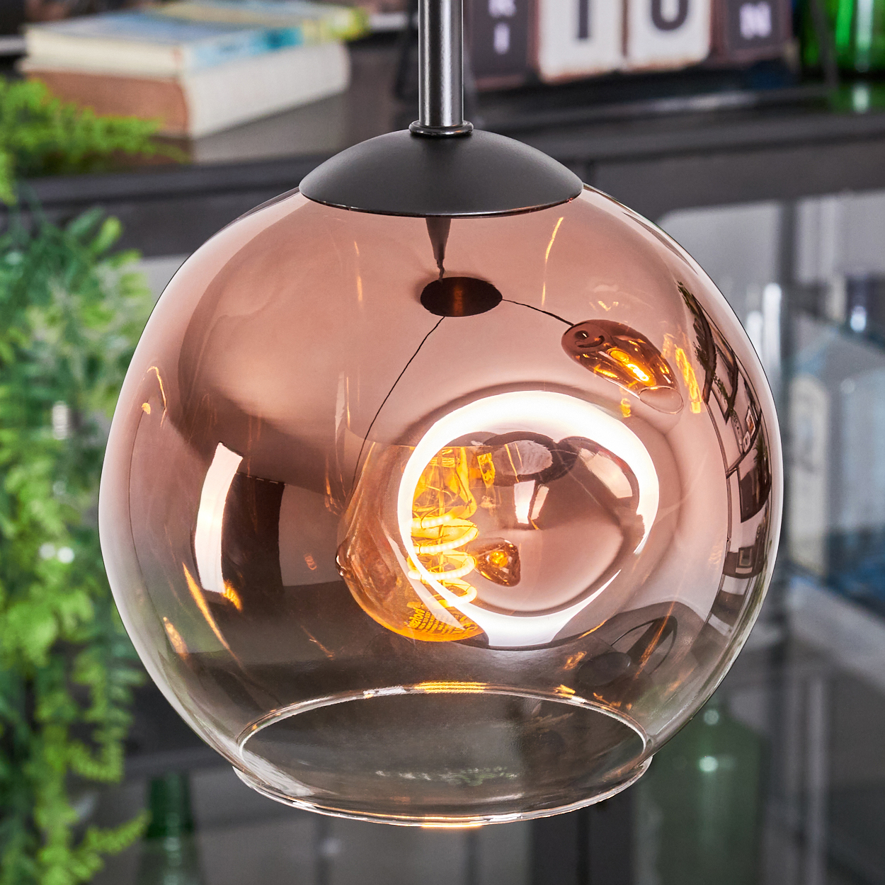 Eine kupferfarbene Glaskugel-Pendelleuchte mit einer leuchtenden, spiralförmigen Glühbirne im Inneren, die an einer schwarzen Halterung hängt.