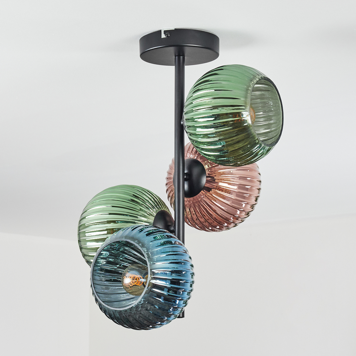 Eine moderne Deckenleuchte mit vier gerippten Glaskugeln in Grün, Rosa und Blau, die an einem schwarzen Metallrahmen hängen.