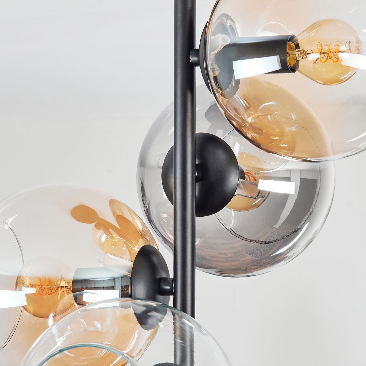 Nahaufnahme einer modernen Lampe. Sie hat klare und bernsteinfarbene Glaskugeln, schwarze Metallakzente und sichtbare Glühbirnen auf weißem Hintergrund.