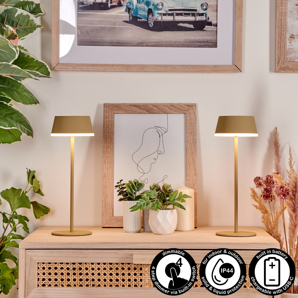 Zwei goldfarbene Lampen auf Holz, mit Pflanzen und gerahmten Bildern im Hintergrund. Merkmale: dimmbar, Akku und USB-C.