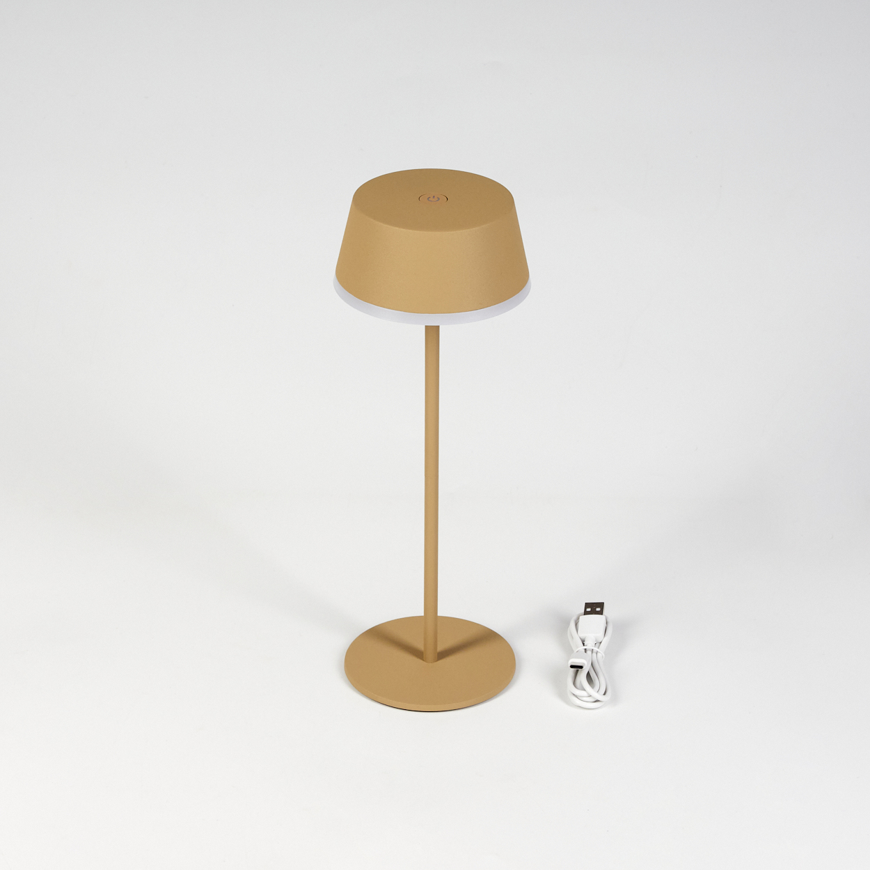 Eine beige Tischlampe steht auf einer weißen Oberfläche. Sie hat einen Lampenschirm, einen langen Stiel und einen runden Fuß. Ein weißes USB-Kabel liegt daneben.