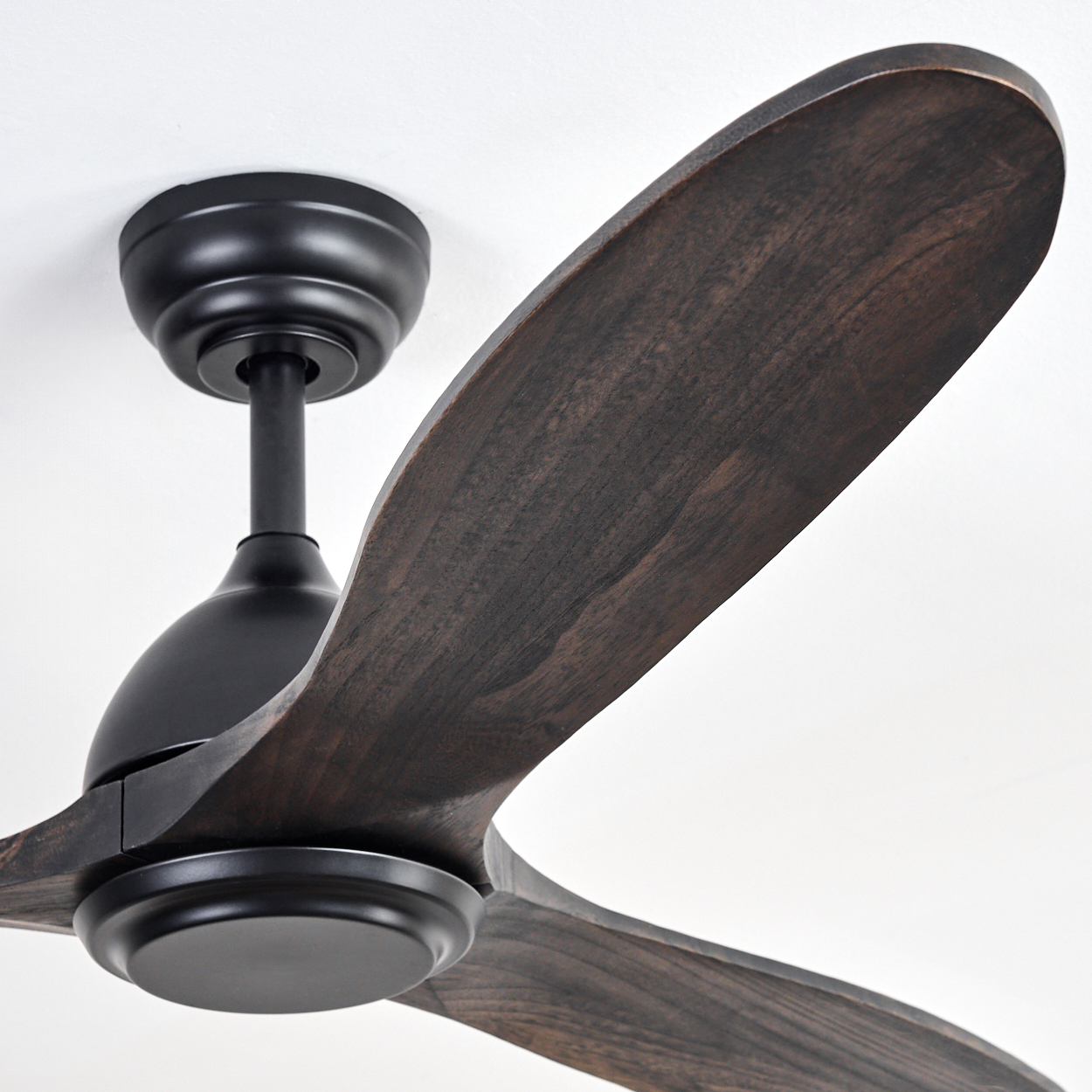 Ein Deckenventilator mit dunkelbraunen Holzflügeln und einem schwarzen Motor vor einer weißen Decke.