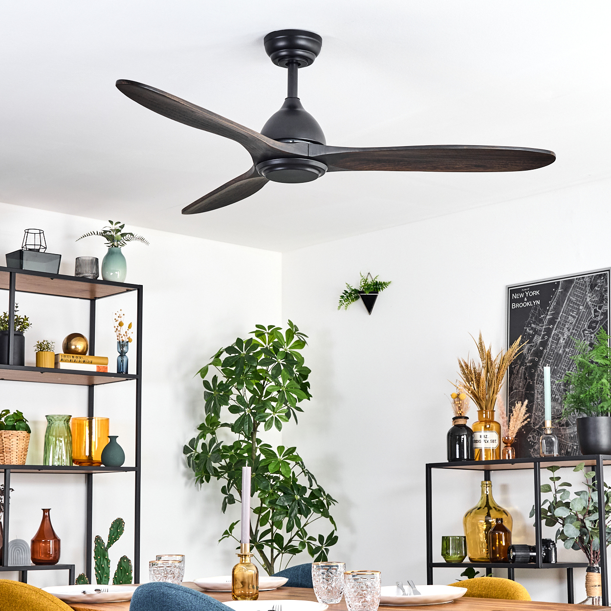 Ein modernes Esszimmer. Ein schwarzer Deckenventilator mit Holzblättern. Der Tisch ist zum Abendessen gedeckt, mit Pflanzen und Regalen mit Dekorationen.