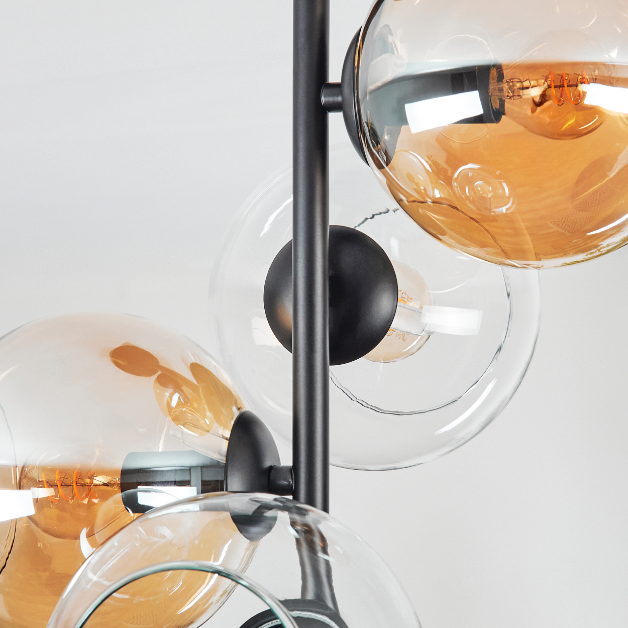 Nahaufnahme einer modernen Lampe mit mehreren Glaskugeln in Bernstein und klar. Schwarzer Metallrahmen. Weißer Hintergrund.