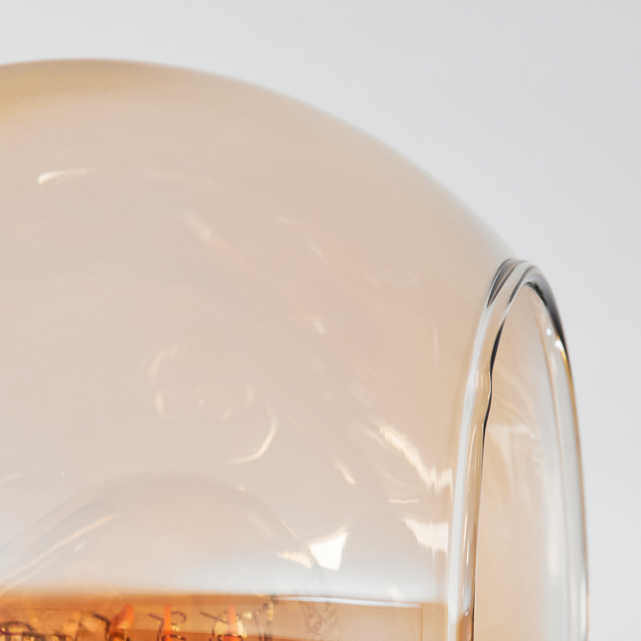 Nahaufnahme eines gläsernen Lampenschirms mit glatter, gewölbter Oberfläche. Das Glas hat eine hellbernsteinfarbene Farbe, vor weißem Hintergrund.