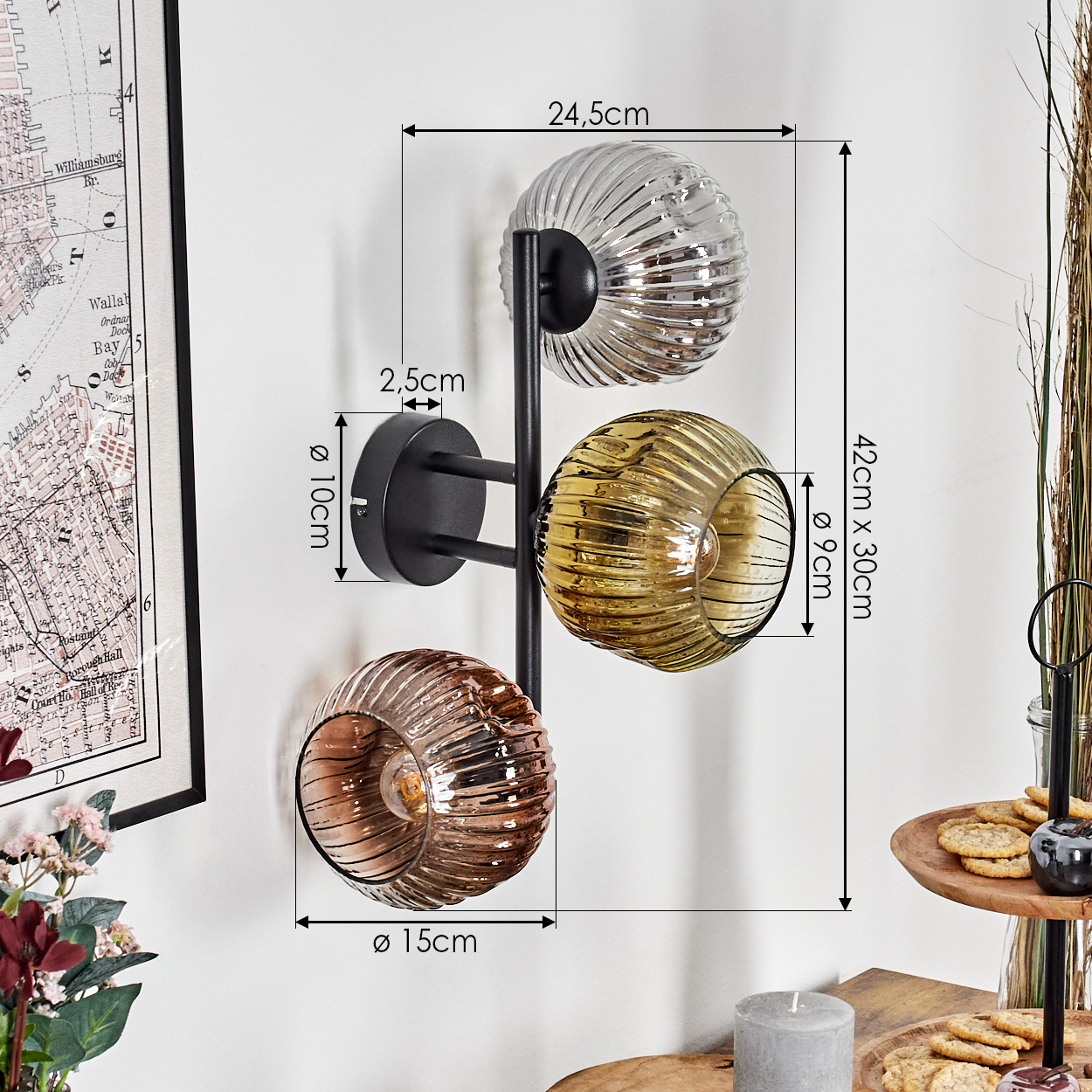 Eine Wandlampe mit drei Glaskugeln in verschiedenen Farben ist an einer weißen Wand befestigt. Abmessungen sind neben der Lampe angegeben.