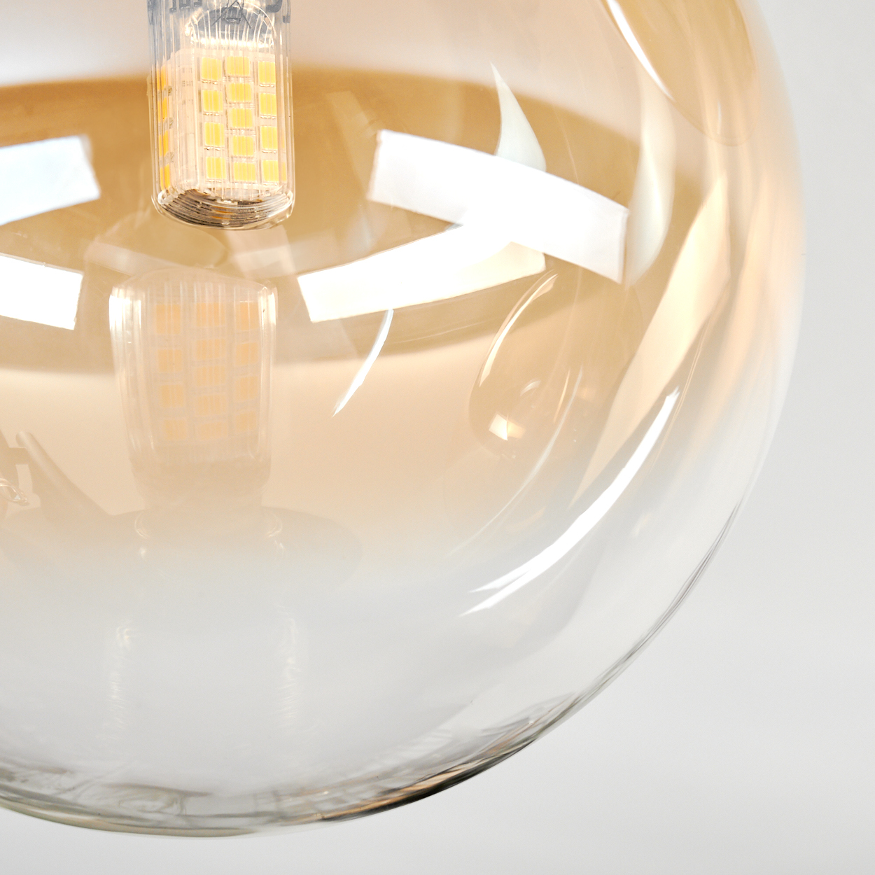 Nahaufnahme einer dekorativen Glühbirne. Die Birne ist eine transparente Kugel mit einem Farbverlauf von Bernstein nach Weiß. Eine kleine LED ist sichtbar.