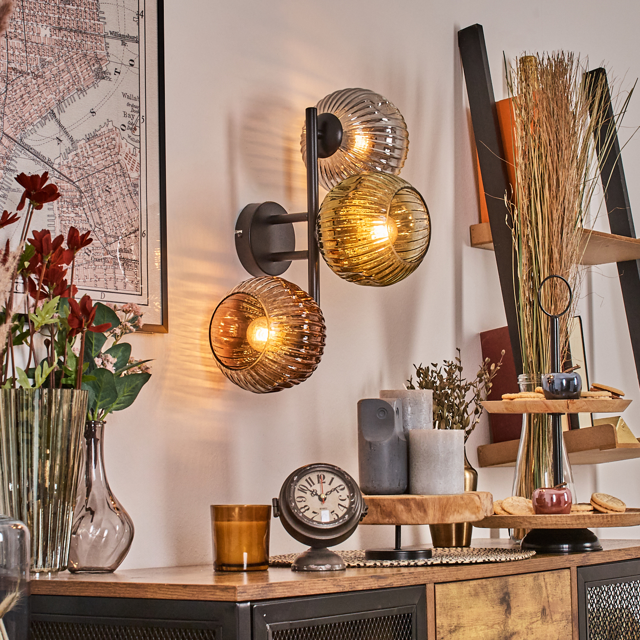 Eine Wand mit einer Lampe, einer Karte und Dekoration. Ein Holzregal mit Kerzen, einer Uhr und einer Leiter mit Büchern.