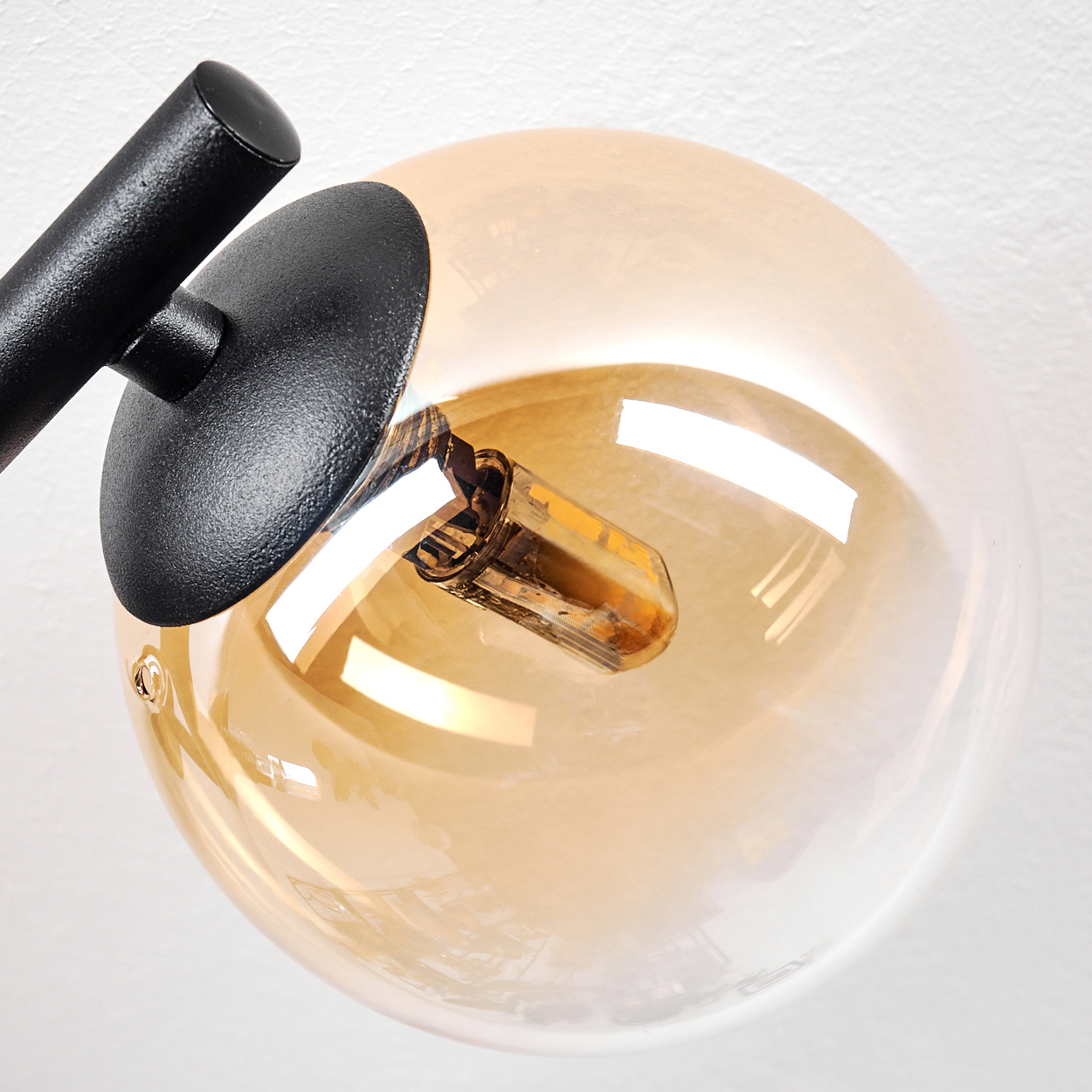Nahaufnahme einer modernen Lampe. Sie hat einen schwarzen Arm und einen runden, klaren Glasschirm mit einer Glühbirne. Der Hintergrund ist weiß.