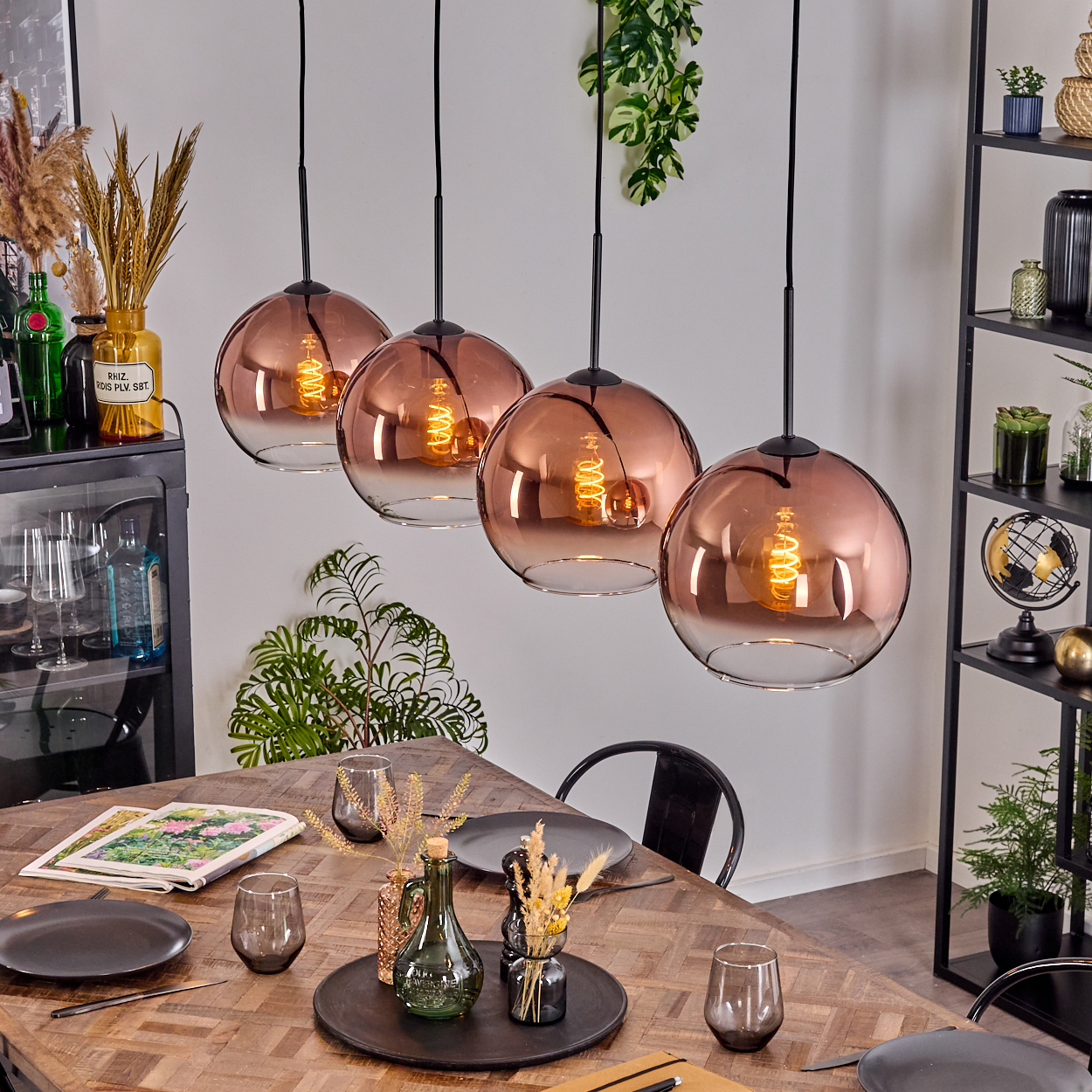 Esszimmer mit vier kupferfarbenen Pendelleuchten. Ein Holztisch ist mit Tellern und Gläsern gedeckt. Regale mit Deko befinden sich rechts.