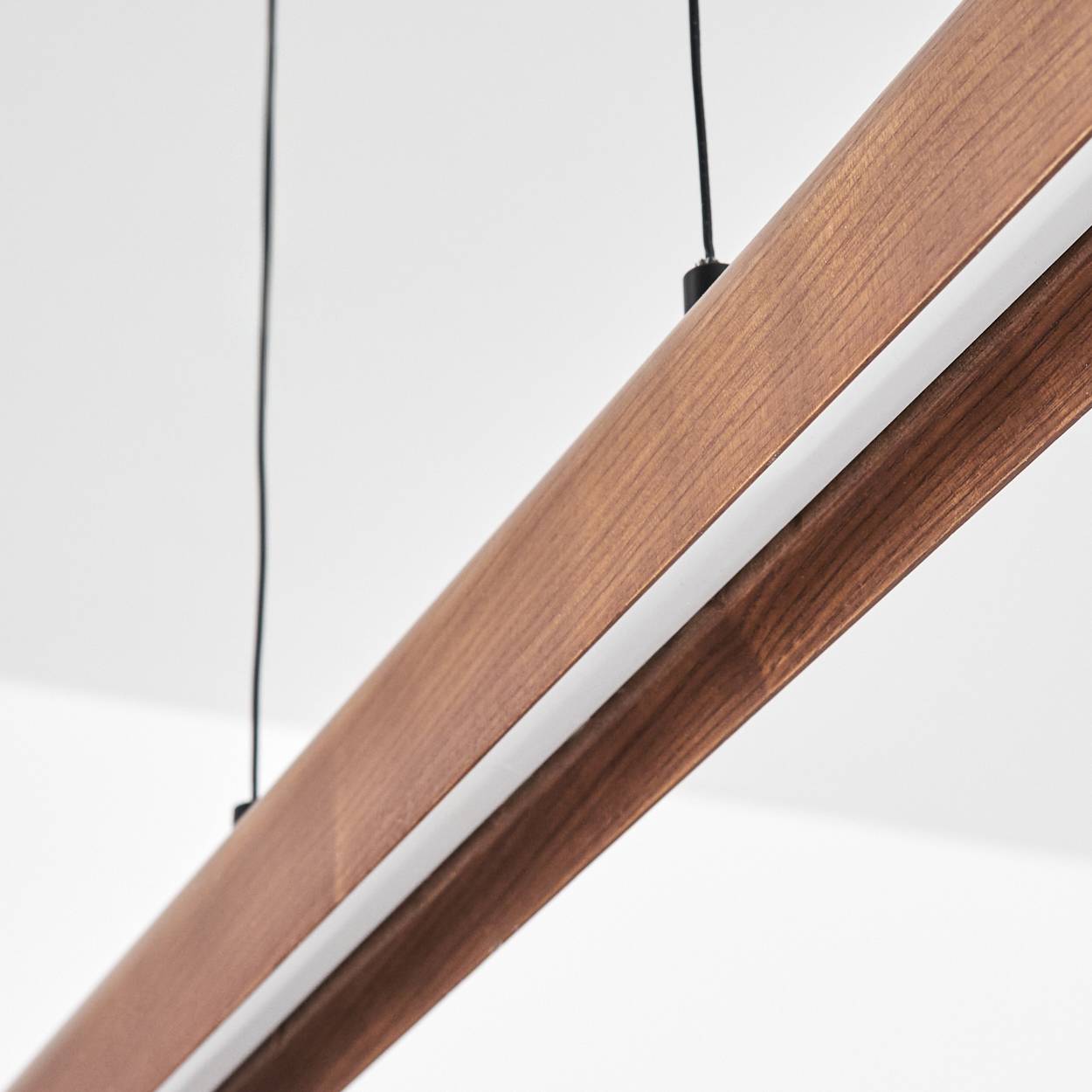 Nahaufnahme einer Holzleuchte mit weißem Lichtstreifen. Schwarze Drähte hängen von der Decke. Der Hintergrund ist weiß.