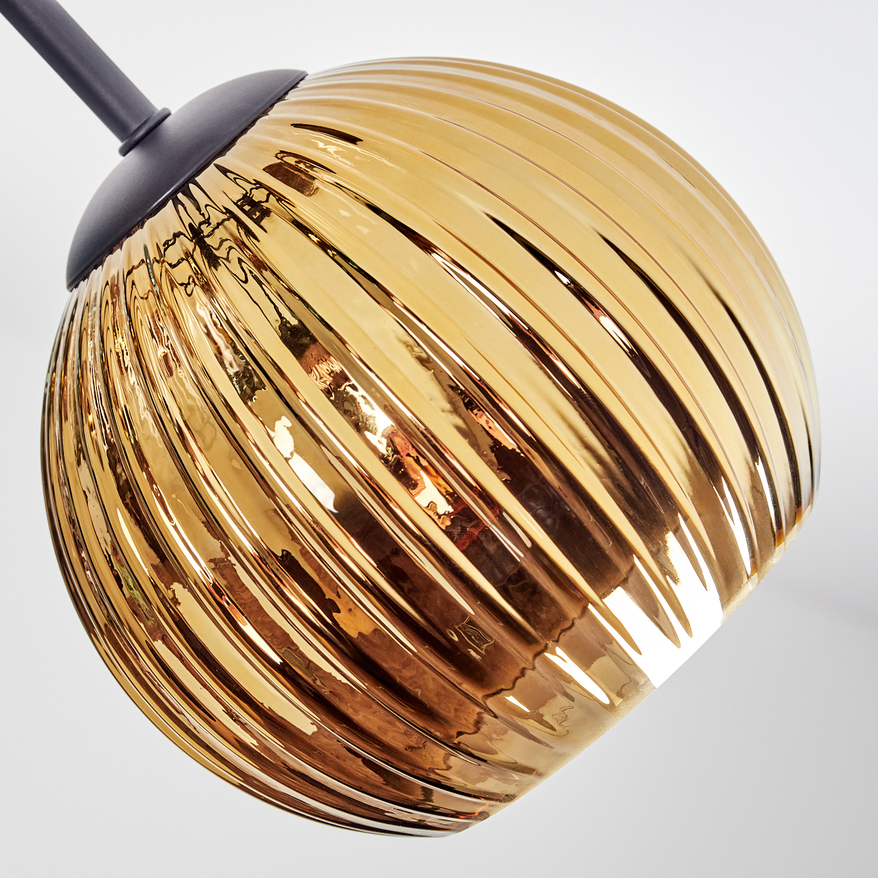 Ein goldener, gerippter Glasschirm hängt vor einem weißen Hintergrund und ist an einer dunkelgrauen Halterung befestigt.