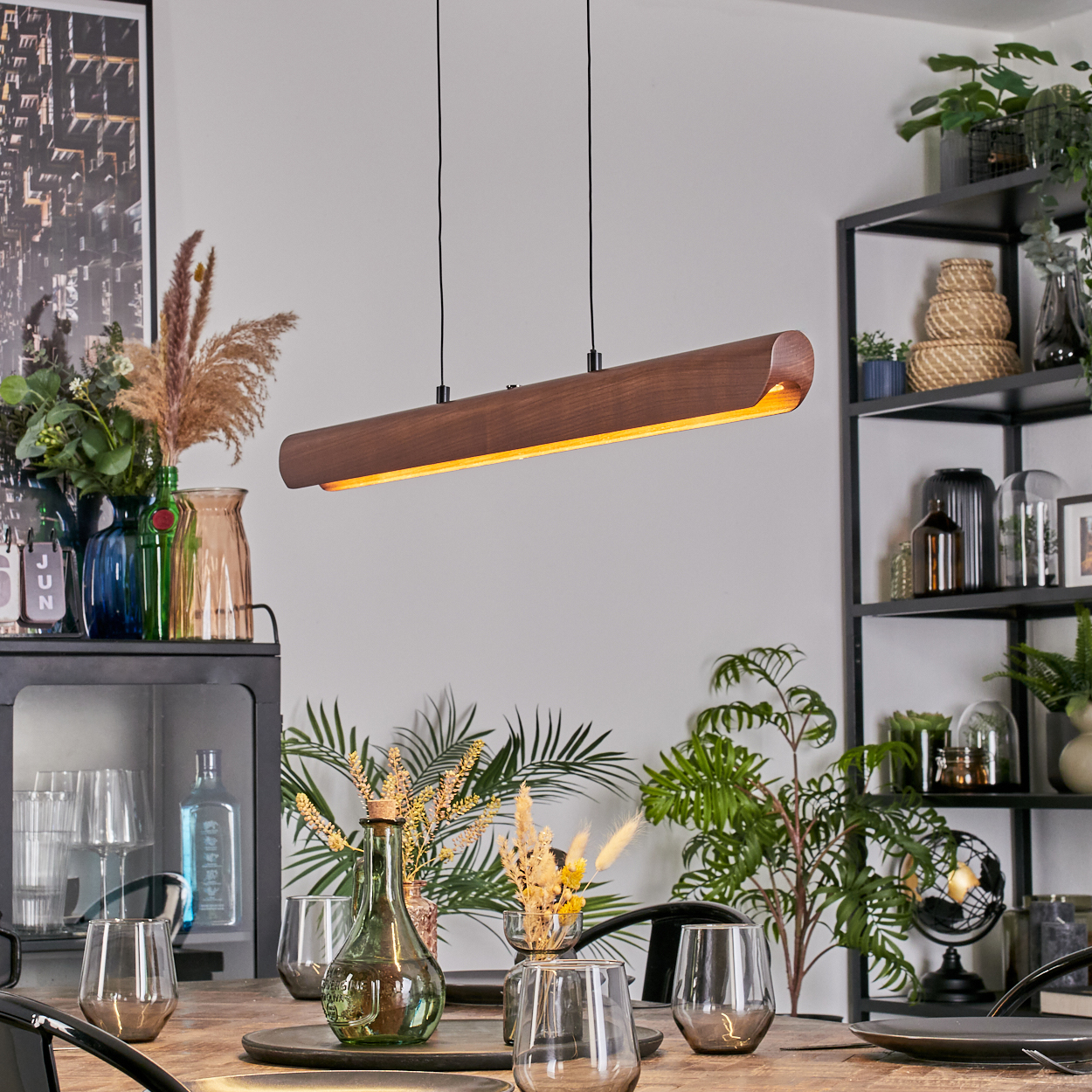 Ein Esszimmer mit einer Holzlampe, Tischdeko und Pflanzen. Im Hintergrund ein schwarzes Regal mit weiteren Pflanzen und Dekorationen.