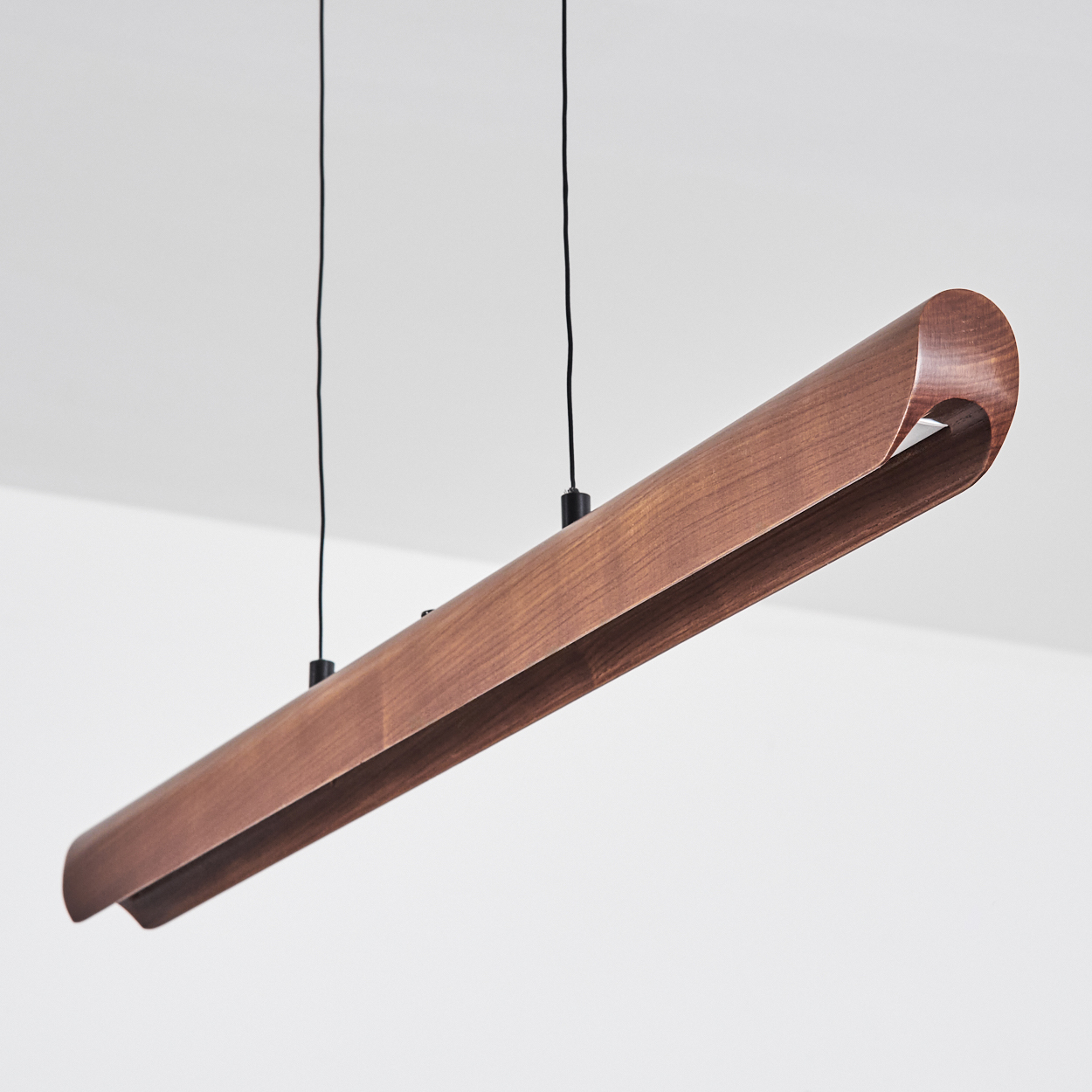 Eine moderne Holzleuchte hängt von der Decke. Sie ist braun, hat ein gebogenes Design und wird von schwarzen Drähten gehalten.