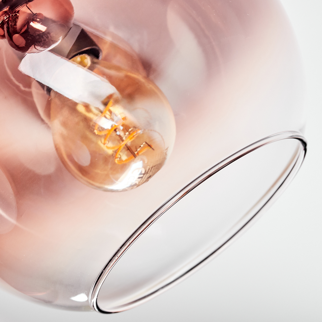 Nahaufnahme einer Leuchte mit einer Glühbirne in einem Glasschirm. Der Schirm hat einen rosafarbenen Farbton und ist teilweise transparent.