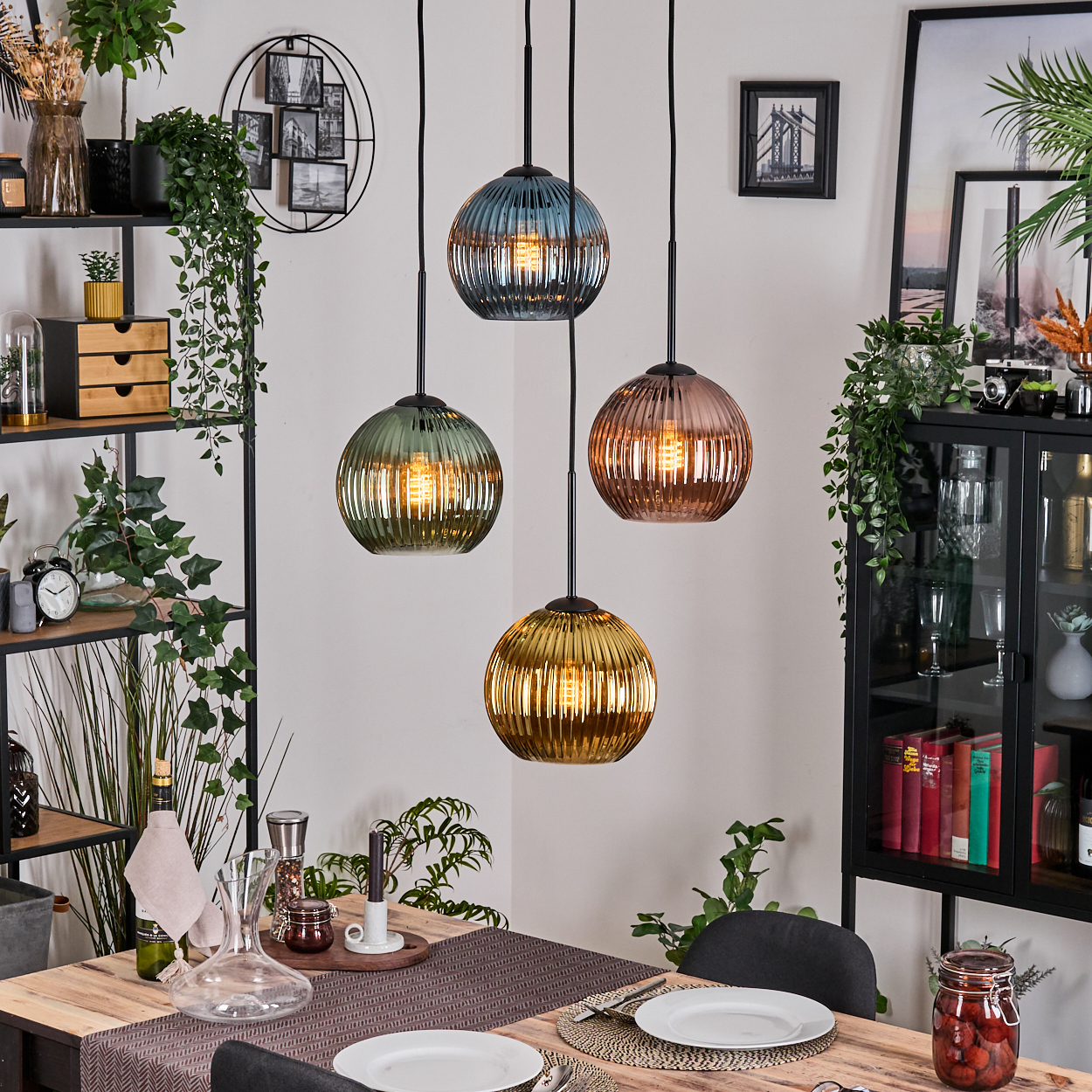 Vier bunte Pendelleuchten über einem Holztisch. Regale mit Pflanzen und Dekorationen sind im Hintergrund.