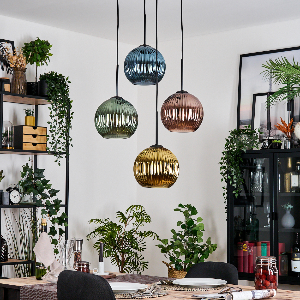 Esszimmer mit vier bunten Pendelleuchten. Pflanzen, Tischgedeck und schwarze Regale sind ebenfalls sichtbar.