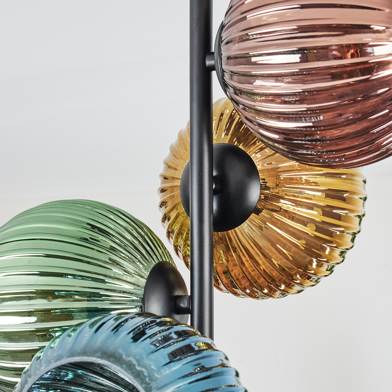 Nahaufnahme einer Lampe mit farbigen Glaskugeln: Kupfer, Gold, Grün und Blau. Schwarze Stützstruktur.