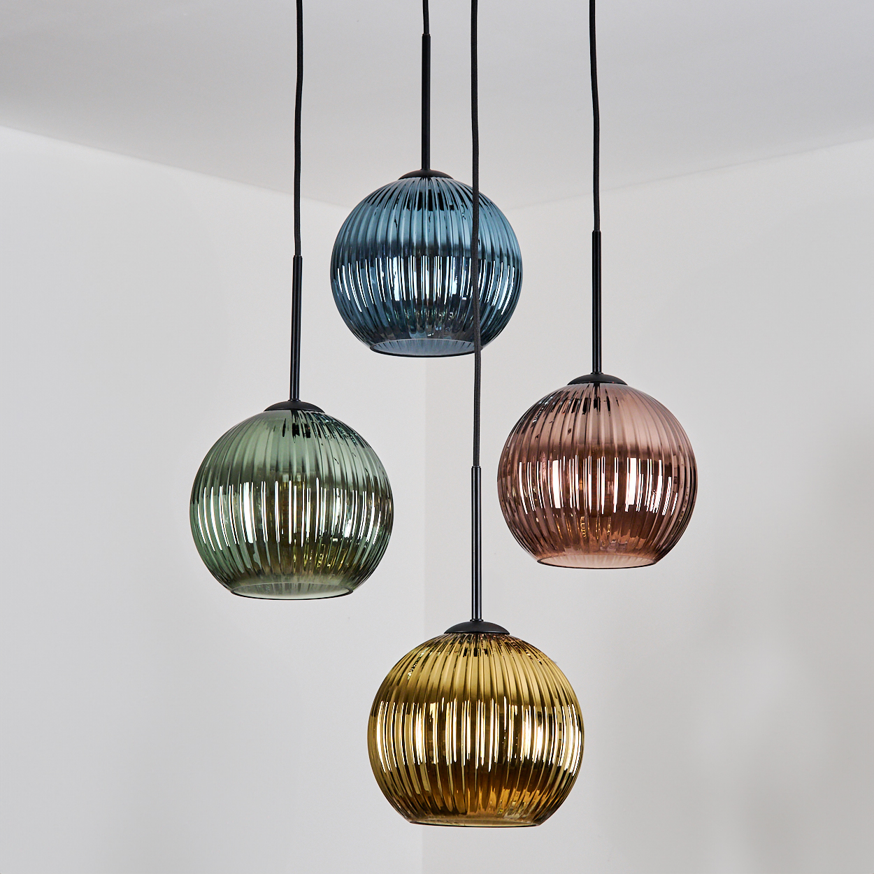 Vier bunte, kugelförmige Pendelleuchten hängen in einer Ecke. Farben sind Grün, Blau, Gold und Rosa, mit schwarzen Kabeln.