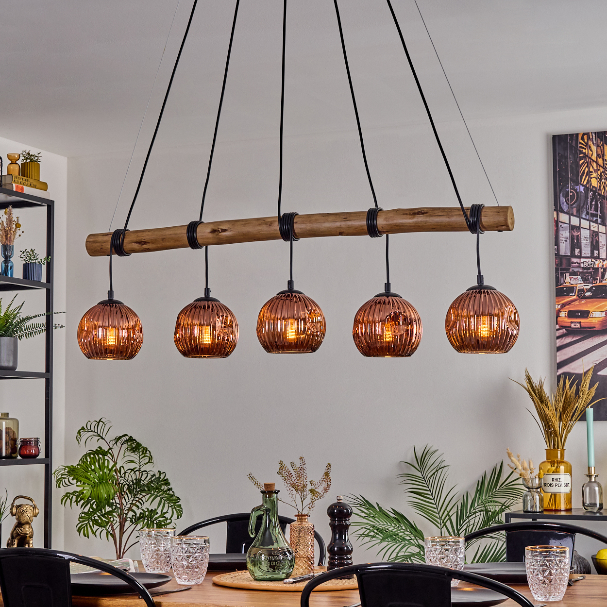 Esszimmer mit Holztisch. Eine Lampe mit fünf Glaskugeln hängt darüber. Pflanzen und Dekoration befinden sich auf dem Tisch und an den Seiten.