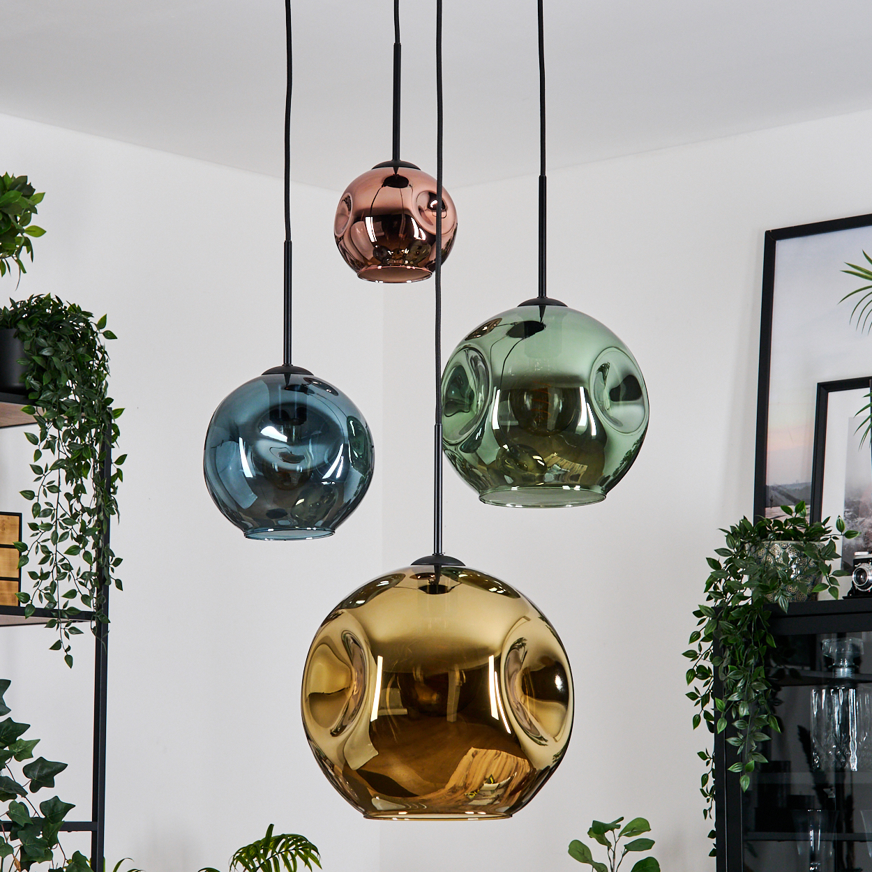 Vier farbige, strukturierte Glas-Hängeleuchten hängen von der Decke. Grüne Pflanzen und Möbel sind im Hintergrund.