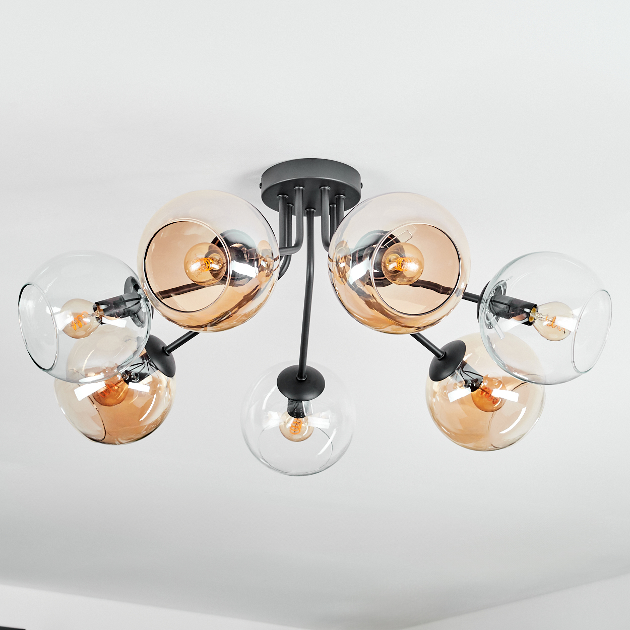 Moderne Deckenleuchte mit sechs Glaskugel-Schirmen, einige bernsteinfarben, hängen von schwarzen Metallarmen. Der Hintergrund ist eine weiße Decke.