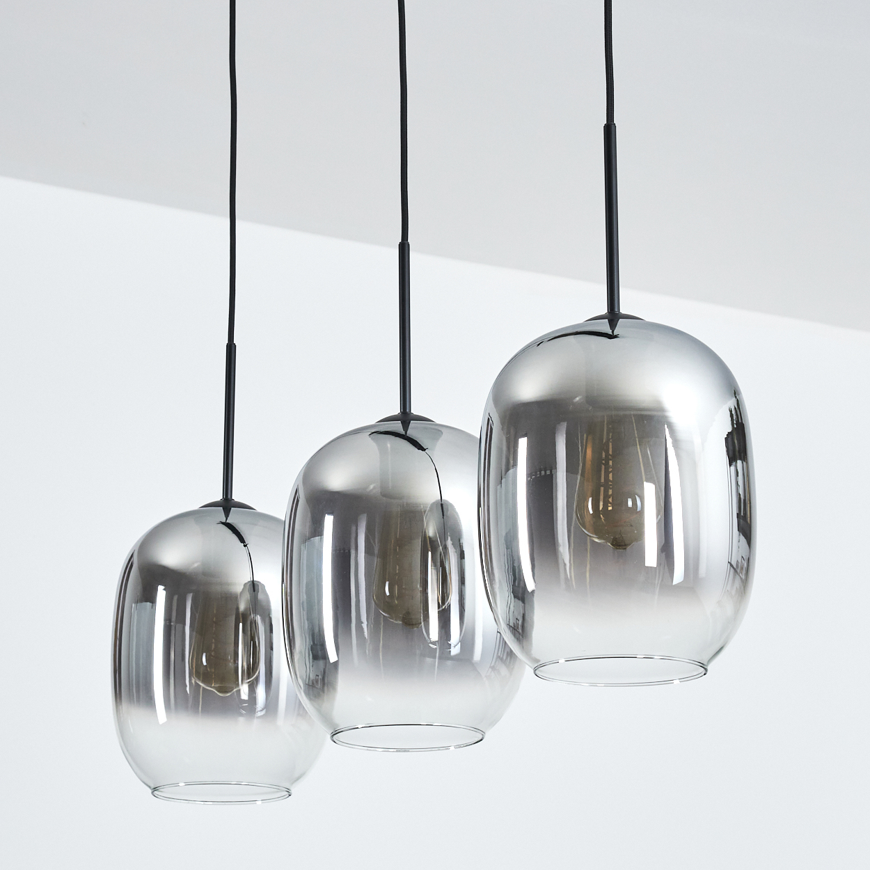 Drei verchromte Pendelleuchten hängen von der Decke. Jede hat einen tropfenförmigen Glasschirm mit einer Glühbirne.