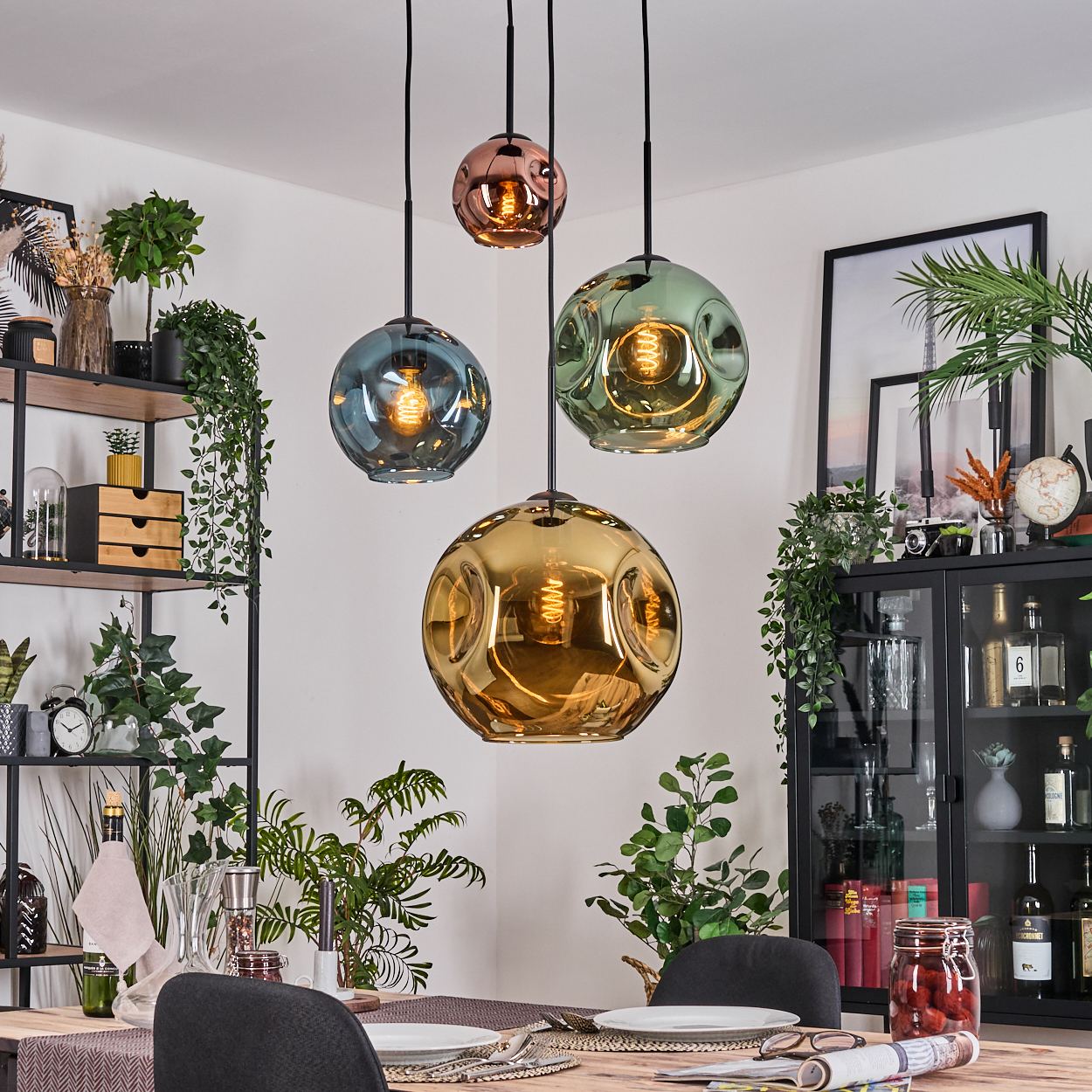 Esszimmer mit vier bunten Pendelleuchten, gedecktem Tisch, Pflanzen und Dekorationsartikeln auf Regalen und Schränken.