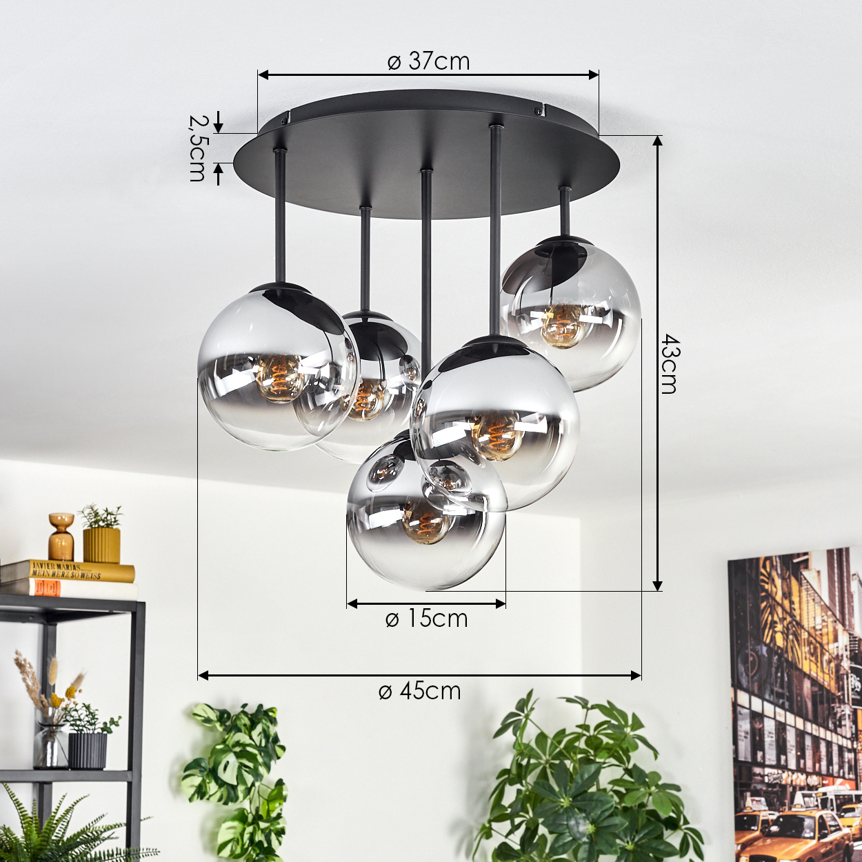 Eine moderne Deckenleuchte mit fünf kugelförmigen Glasschirmen, schwarzer Hardware und beschrifteten Abmessungen. Der Hintergrund zeigt Pflanzen und Kunst.