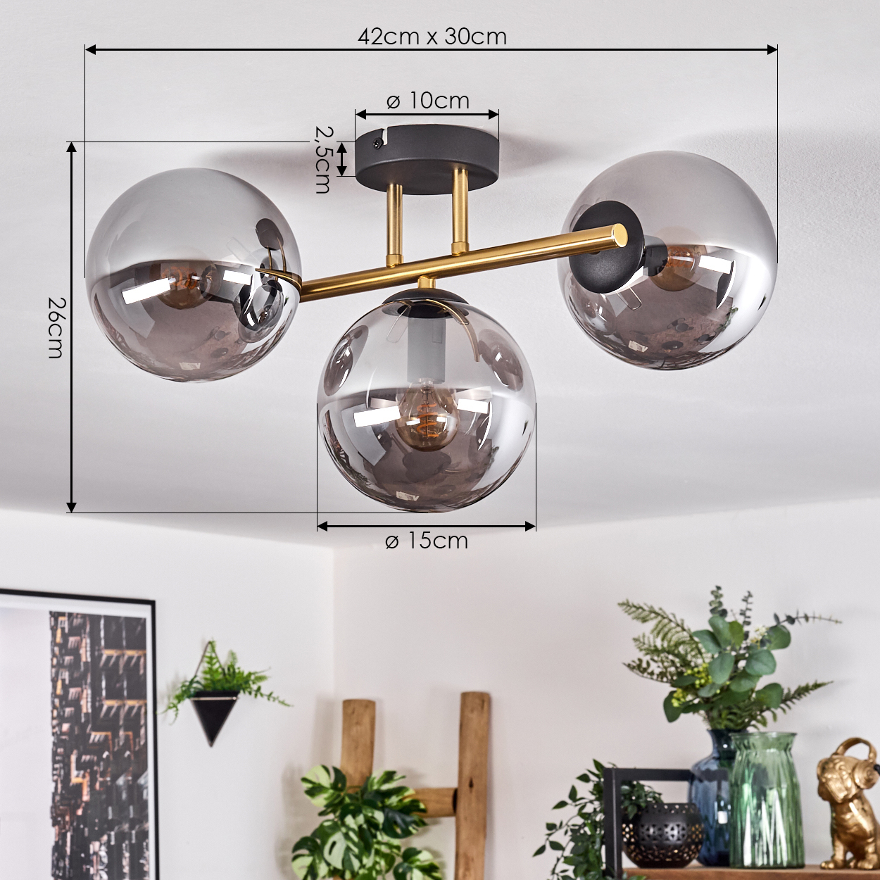 Moderne Deckenlampe mit drei Glaskugeln. Maße sind angegeben. Im Hintergrund ein Regal mit Pflanzen und Dekoration.