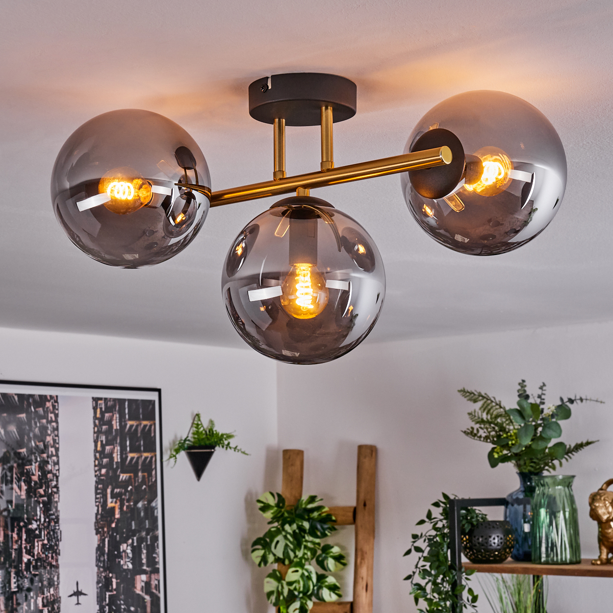 Eine moderne Deckenleuchte mit drei rauchfarbenen Glaskugeln. Jede Kugel hat eine brennende Glühbirne. Die Leuchte ist auf einer Gold- und Schwarzbefestigung montiert.