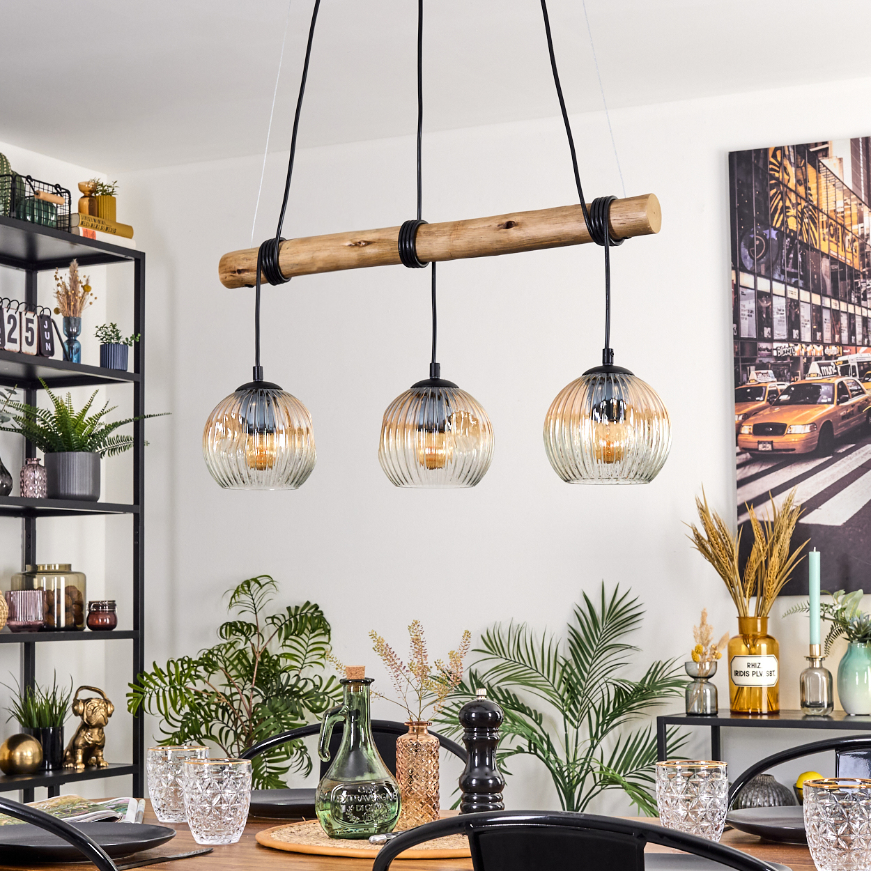 Esszimmer mit Holzbalken und drei Pendelleuchten. Tisch mit Gläsern, Pflanzen und einem Foto von New York City.