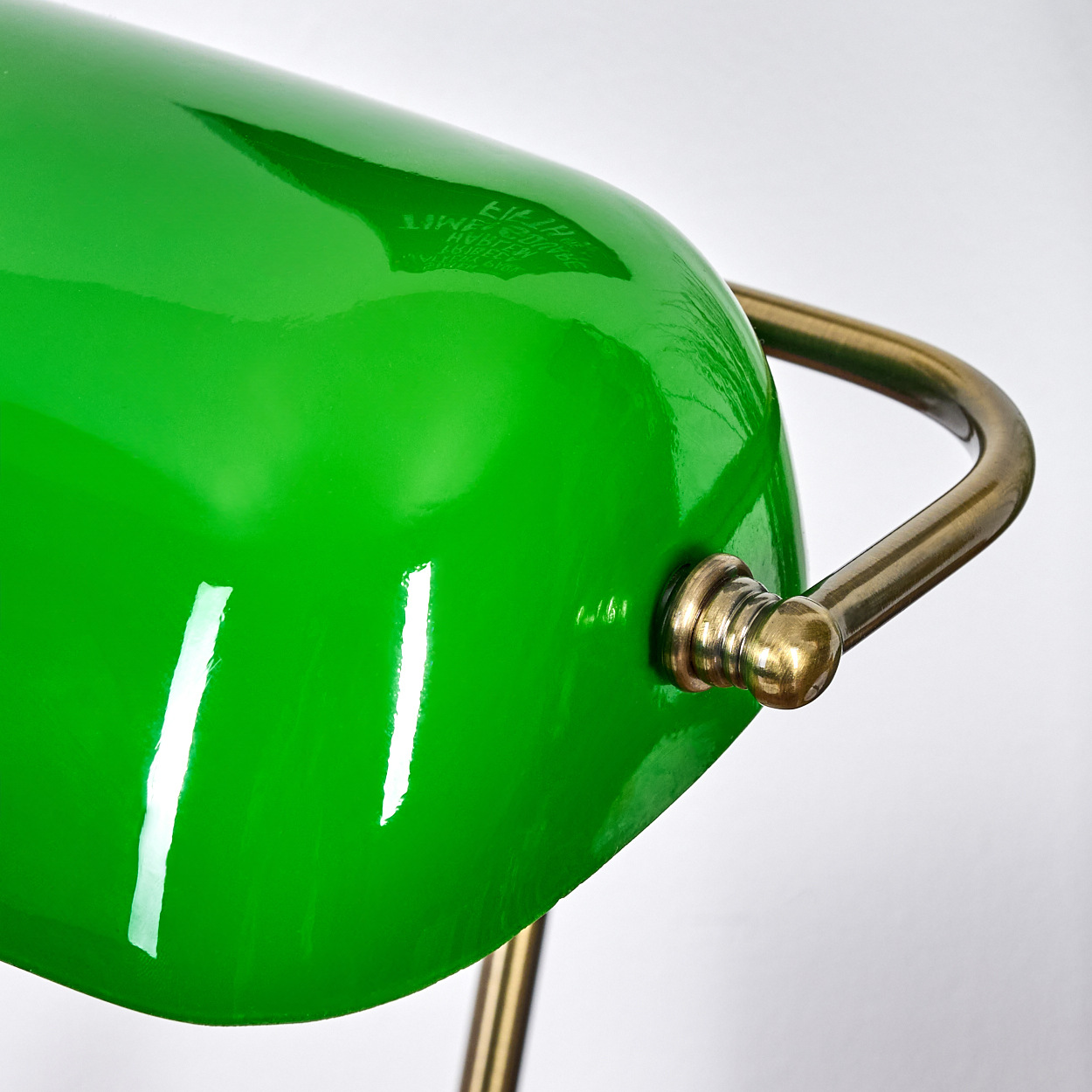 Nahaufnahme einer grünen Schreibtischlampe mit Messinggriff und -fuß, vor weißem Hintergrund.