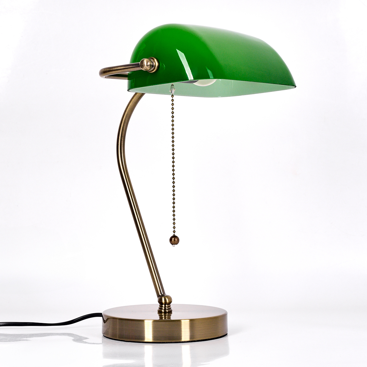 Eine grüne Banker-Lampe mit gebogenem Messingarm. Sie hat einen runden Fuß und eine Zugkette. Der Hintergrund ist weiß.