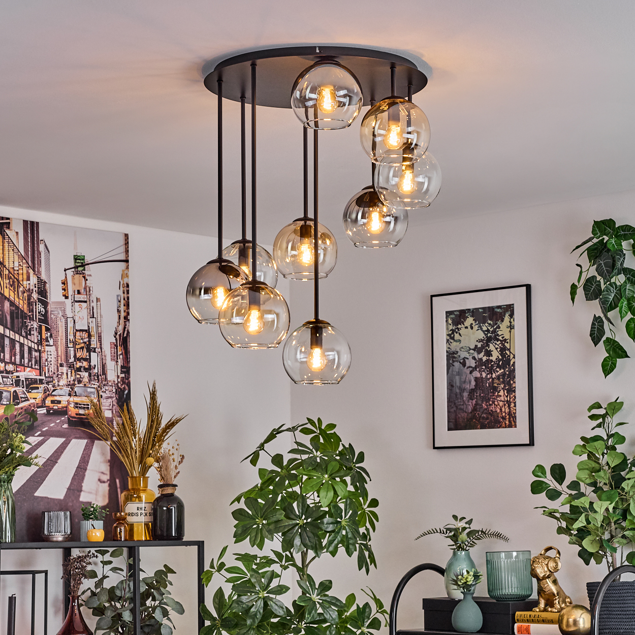 Eine moderne Deckenleuchte mit mehreren Glaskugelleuchten hängt von einer weißen Decke. Pflanzen und Kunstwerke dekorieren den Raum.