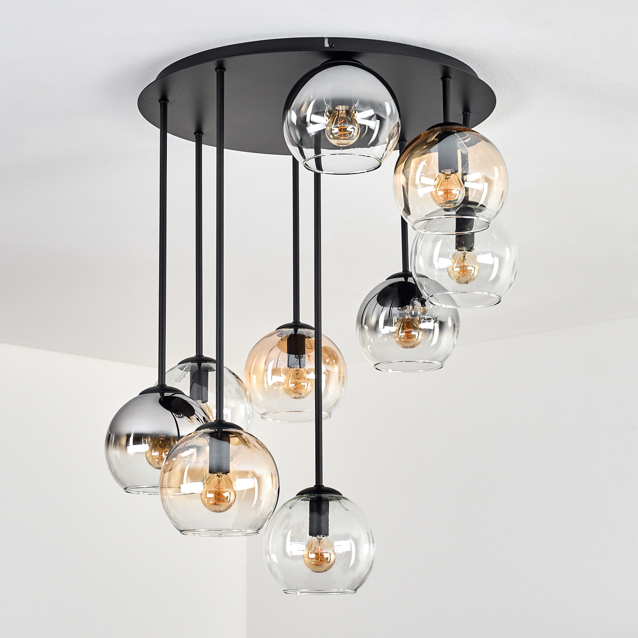 Eine moderne Deckenleuchte mit mehreren kugelförmigen Glasschirmen, jede mit einer Glühbirne. Sie hängt an einer schwarzen Deckenbefestigung.