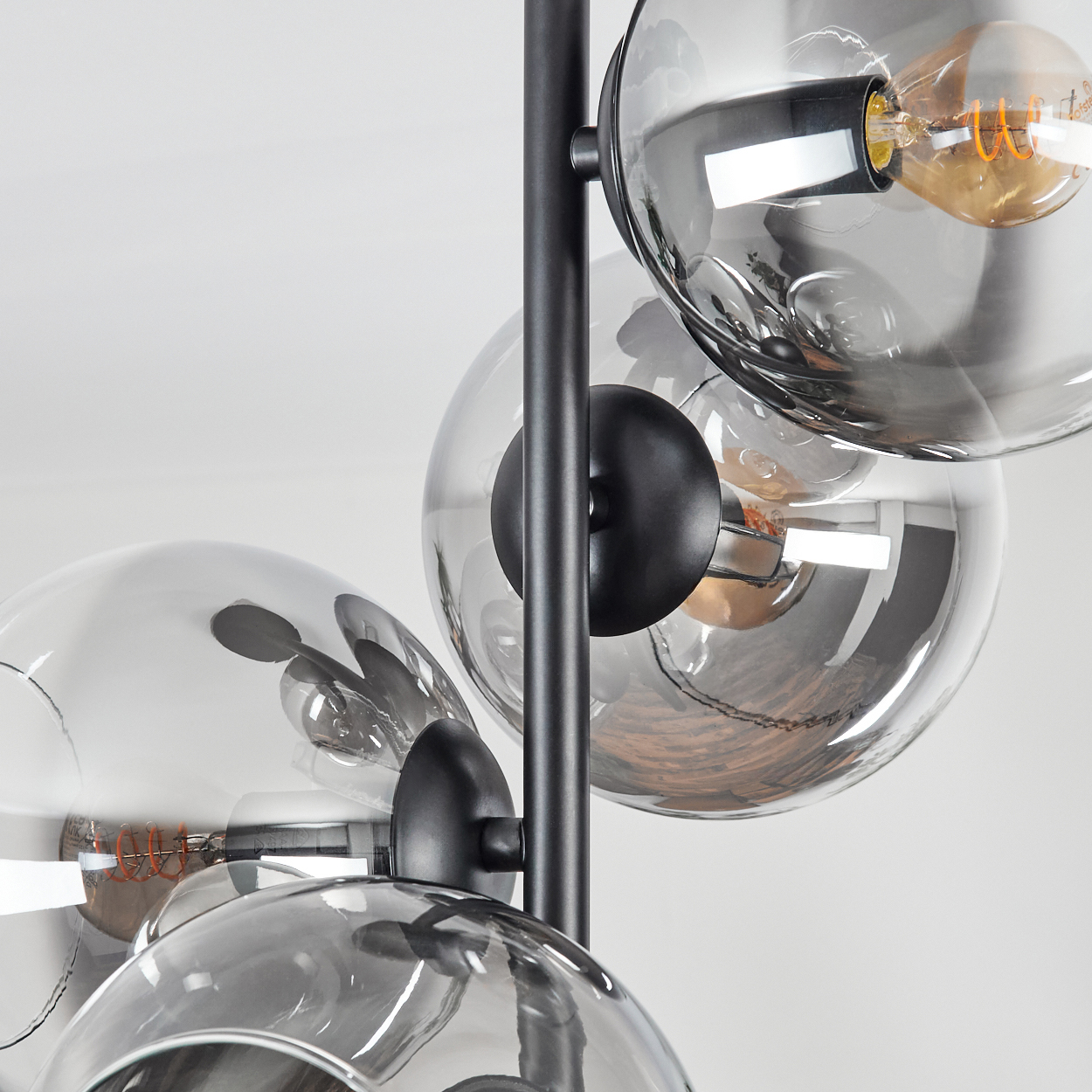 Nahaufnahme einer modernen Lampe mit mehreren Glaskugeln und sichtbaren Glühbirnen. Schwarze Metallstruktur vor weißem Hintergrund.