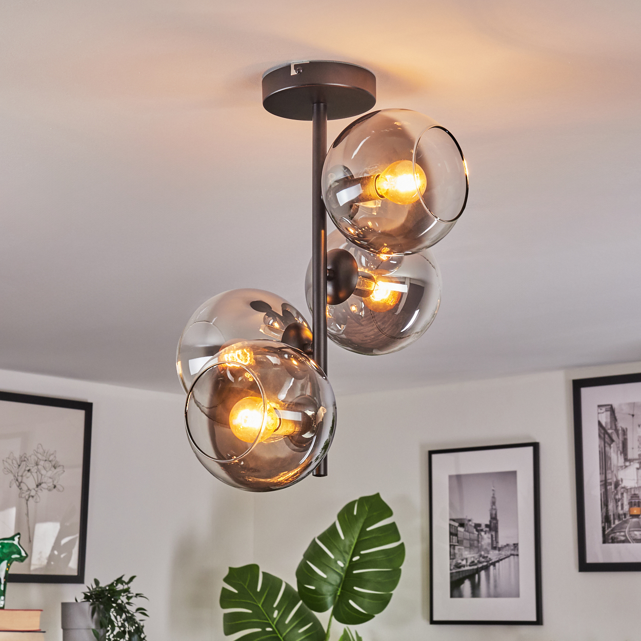 Eine moderne Deckenlampe mit vier Glasschirmkugeln, jede mit einer warmen Glühbirne. Sie ist an einem dunklen Metallrahmen befestigt.