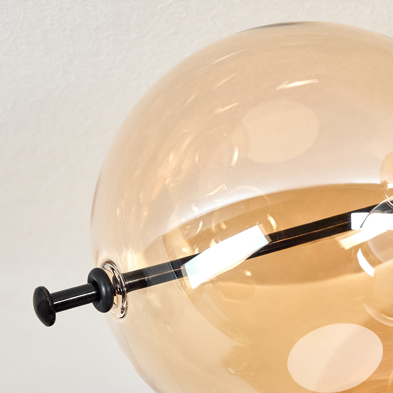 Nahaufnahme einer Glaskugel-Leuchte. Sie hat einen runden, bernsteinfarbenen Glasschirm und schwarze Metalldetails vor weißem Hintergrund.