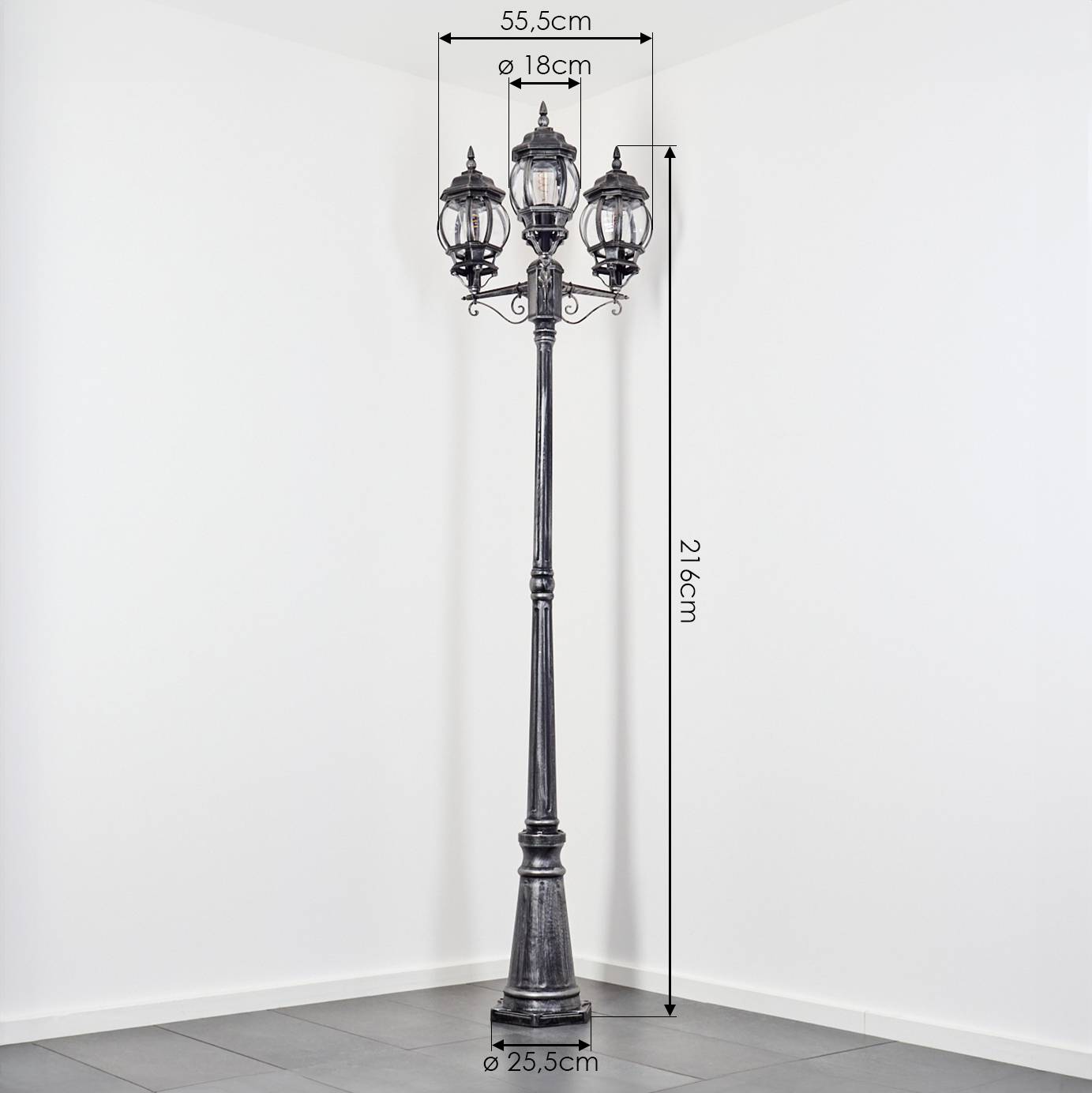 Eine dunkle Metalllaterne mit drei Lampenköpfen. Abmessungen sind angegeben, die Laterne steht an einer weißen Ecke und grau gefliestem Boden.
