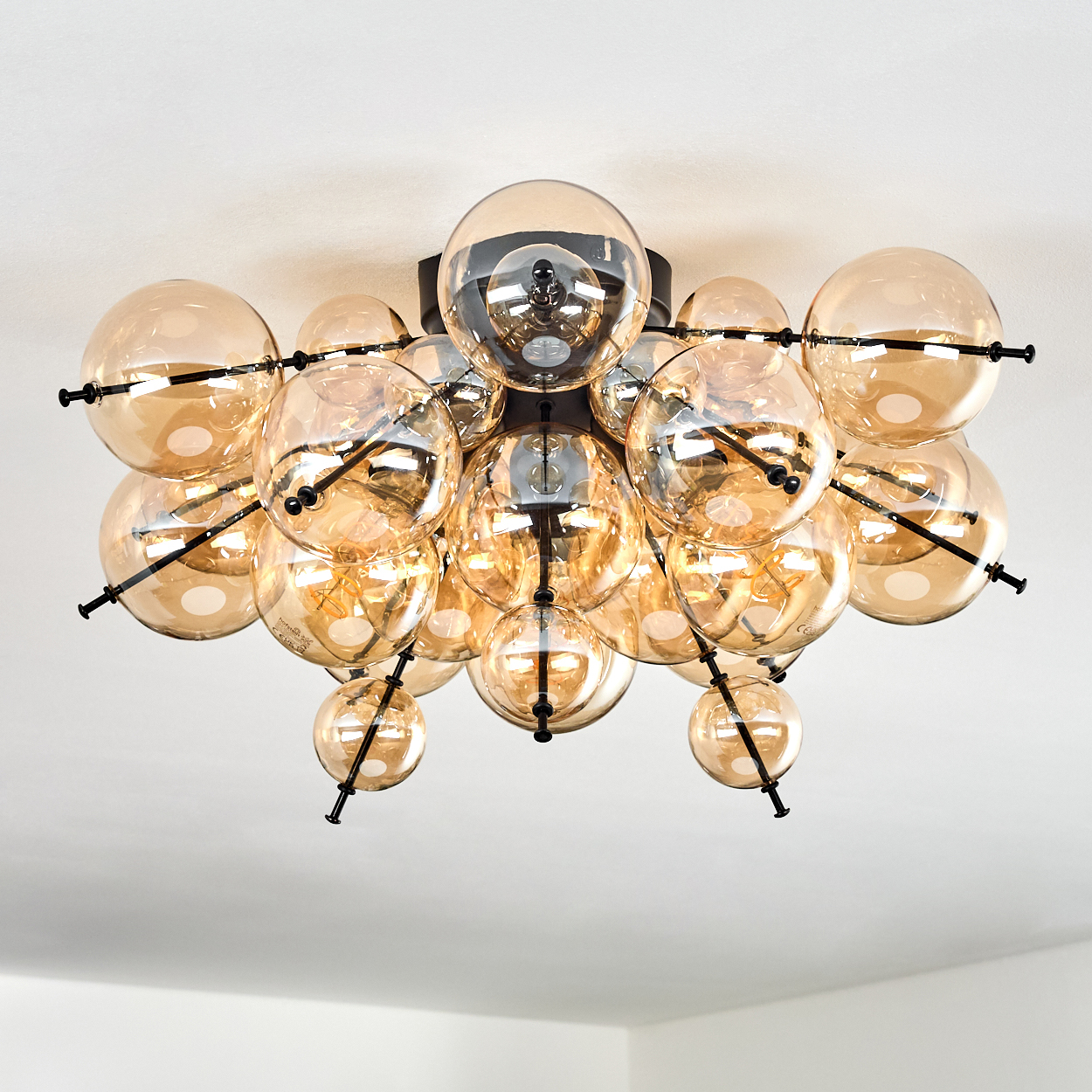Eine moderne Deckenleuchte mit mehreren bernsteinfarbenen Glaskugeln an schwarzen Metallstangen vor weißer Decke.