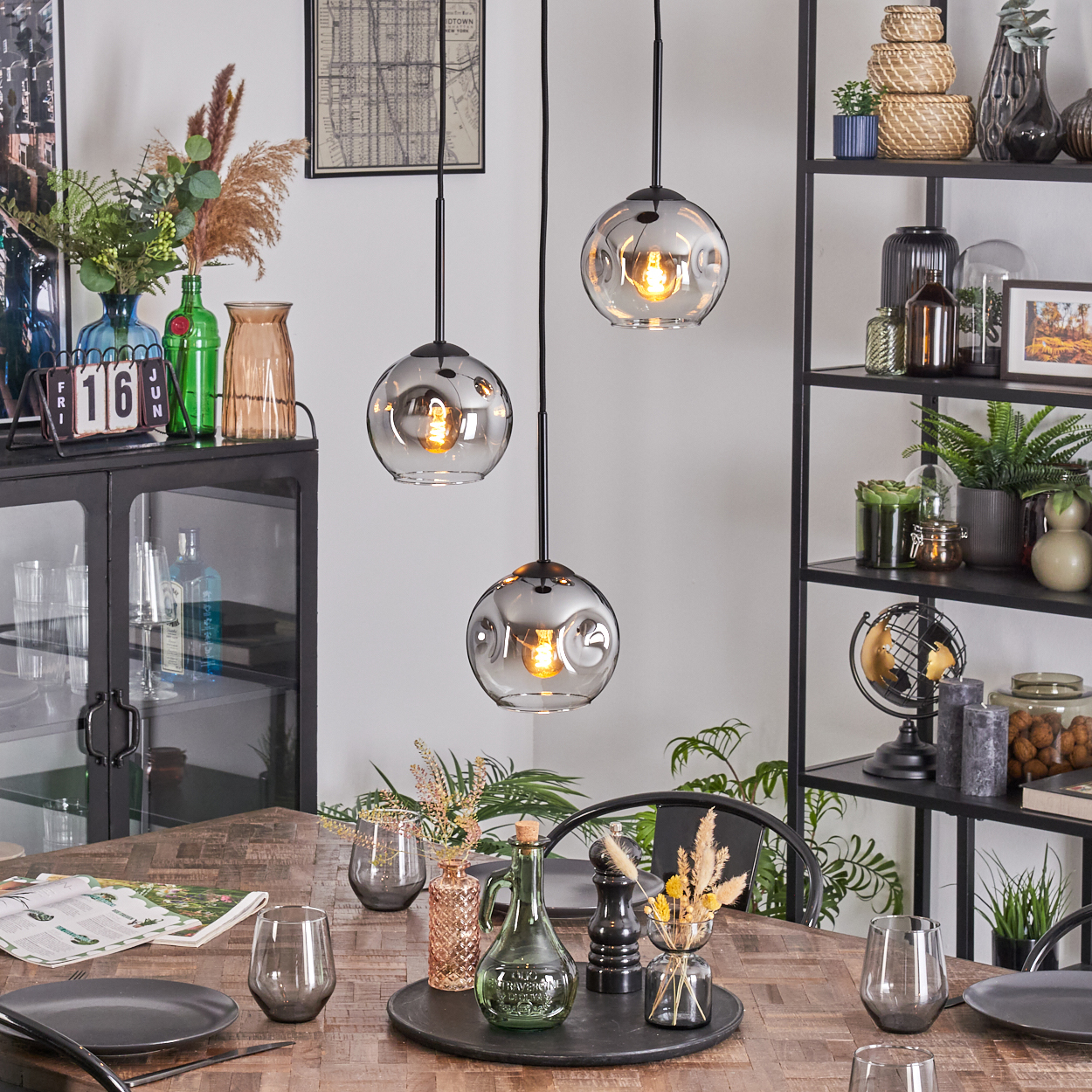 Esszimmer mit Hängelampen, Holztisch, schwarzem Metallregal mit Dekorationen, Vasen und Pflanzen.